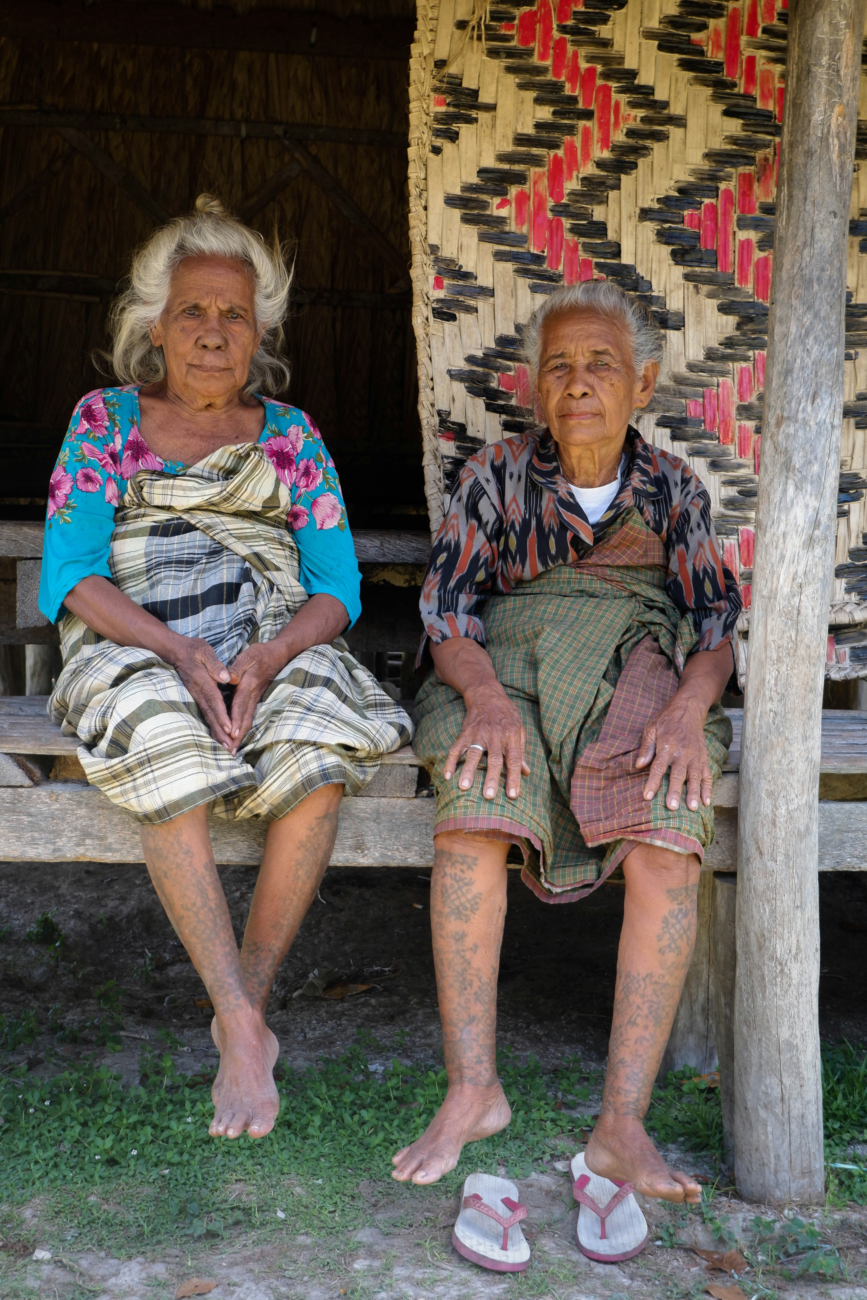 Two elderly people sitting on a bench outdoors.