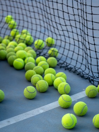 Tennis balls scattered on a hard court near the net, ready for a lesson at a public park