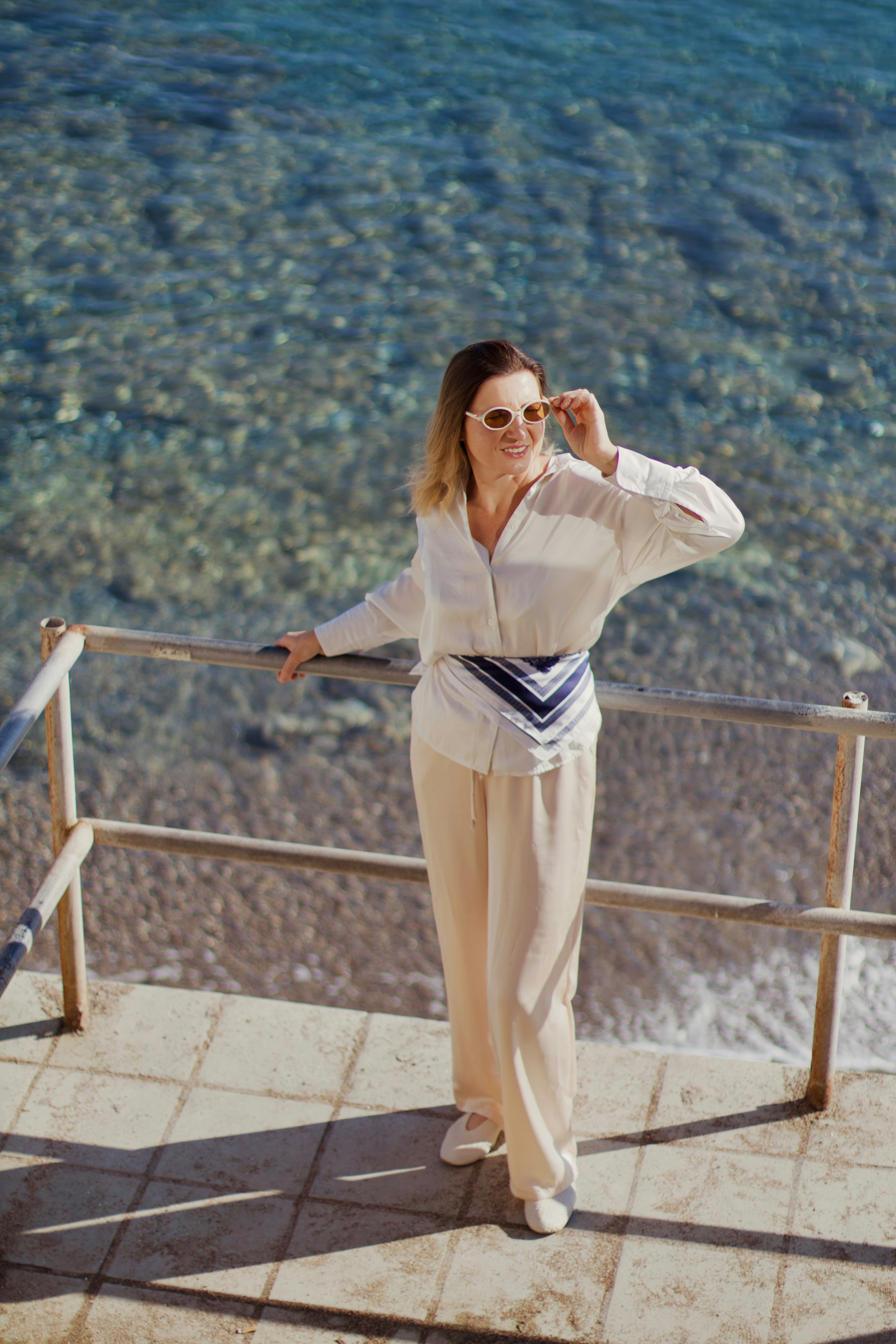 A woman in stylish clothing stands by the ocean.