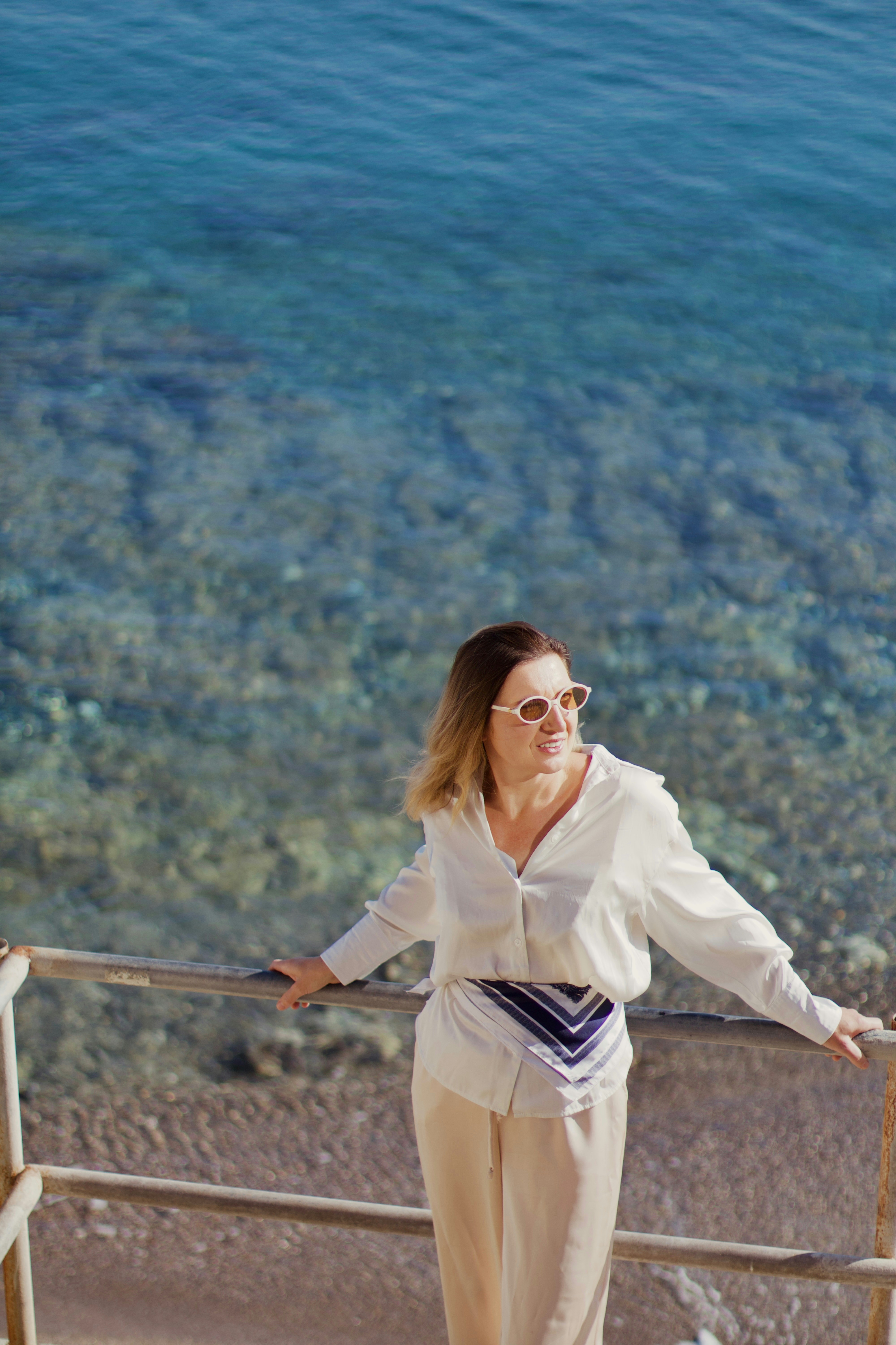 A woman in white stands by the ocean.