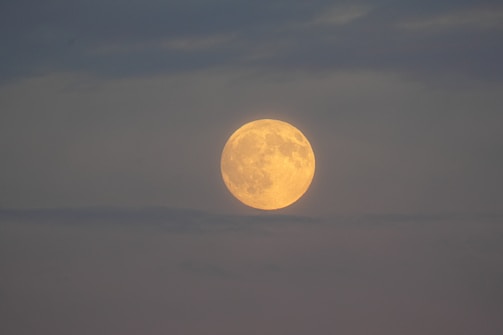 Full moon glowing through hazy clouds at dusk