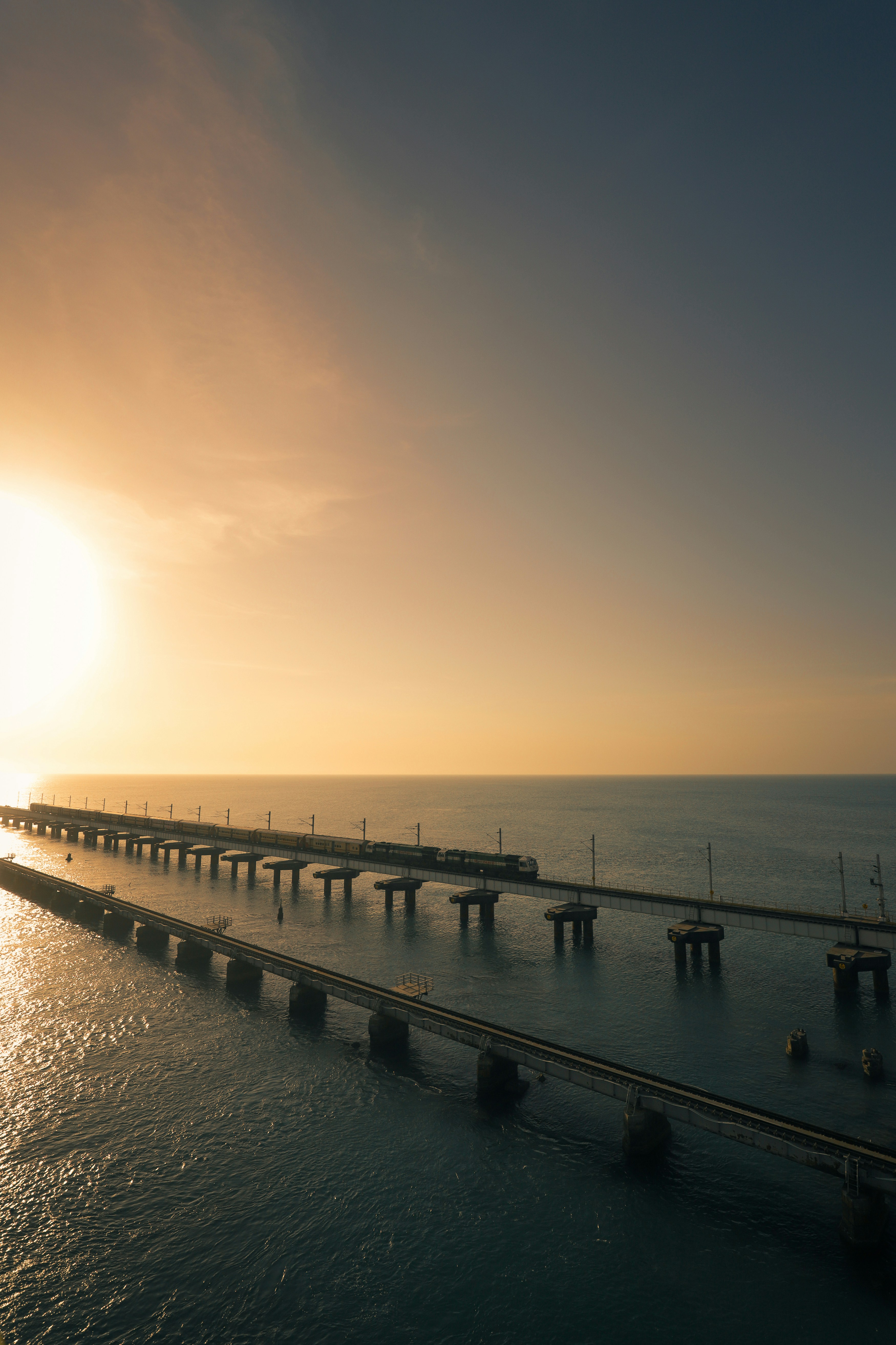 Train crossing a long bridge over the ocean at sunset