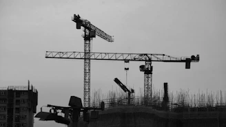 Construction cranes silhouetted against a cloudy sky