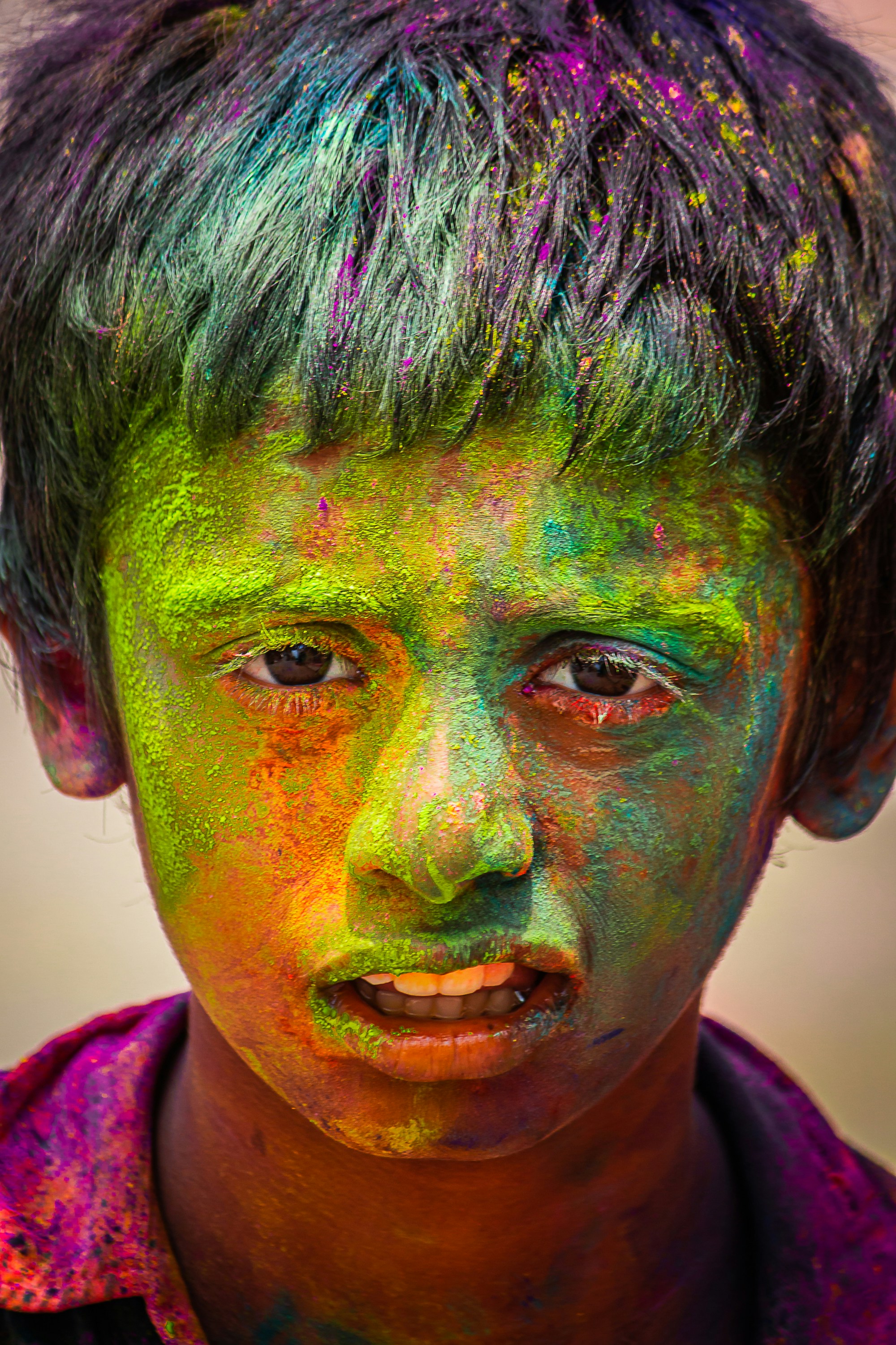 A young boy with his face covered in colorful powder.