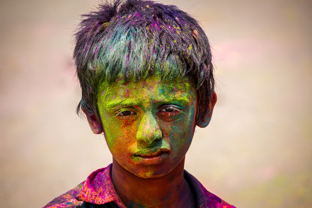Young boy with colorful powder on his face during Holi celebration. Photo by Pavan Prasad on Unsplash.
