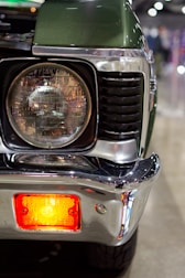Close-up of a vintage green car's headlight and bumper