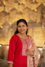 A smiling woman in a red outfit with intricate embroidery.