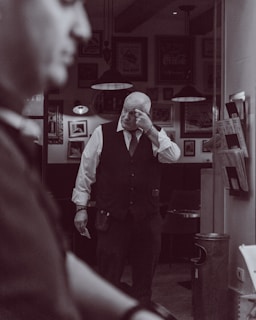Man in vest adjusts glasses in dimly lit room.