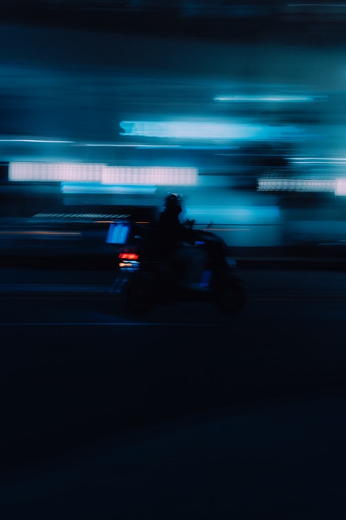 Blurry silhouette of a person riding a scooter at night