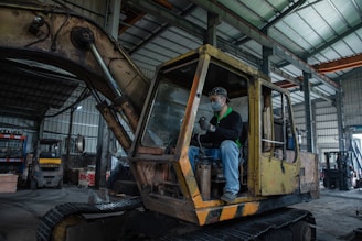 Man sits in an old excavator in a workshop.