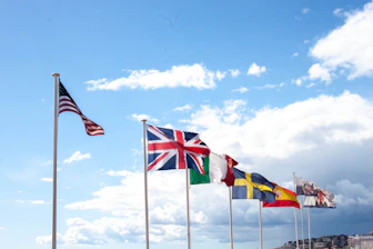Several national flags flying against a cloudy sky.