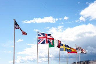 Several national flags flying against a cloudy sky.