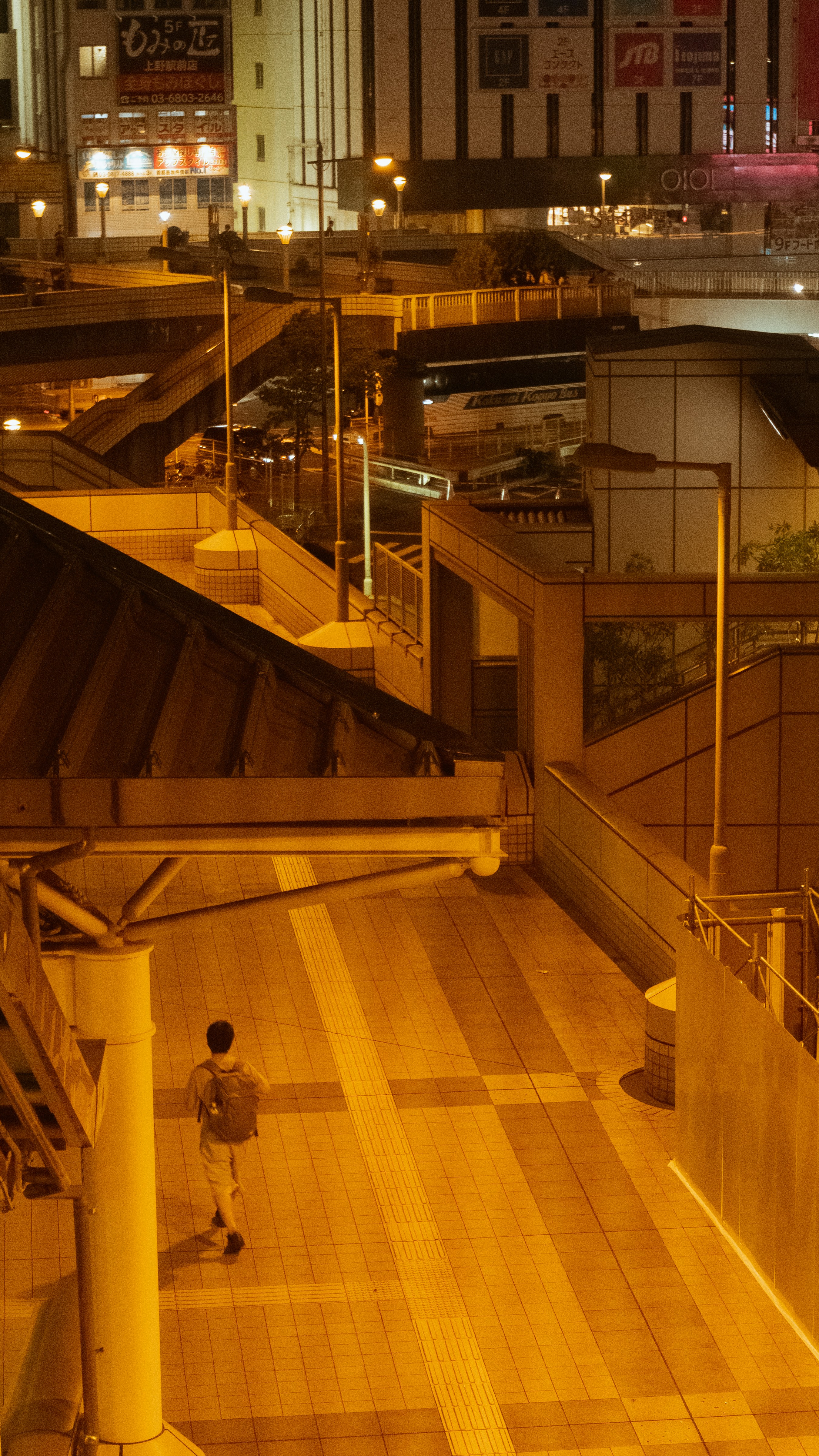 Man with backpack walks on illuminated city walkway at night.