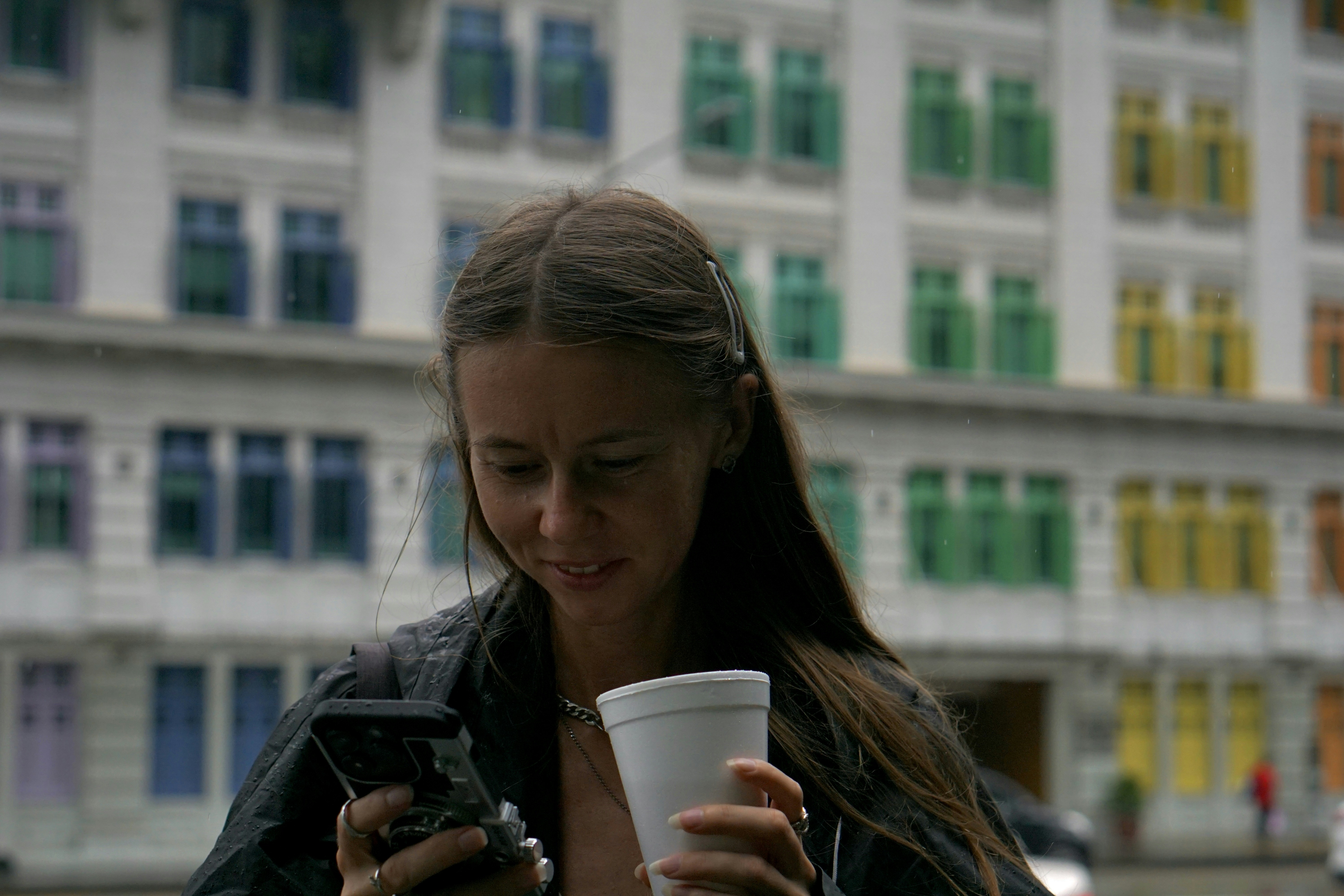 Mujer sosteniendo una bebida y mirando el teléfono
