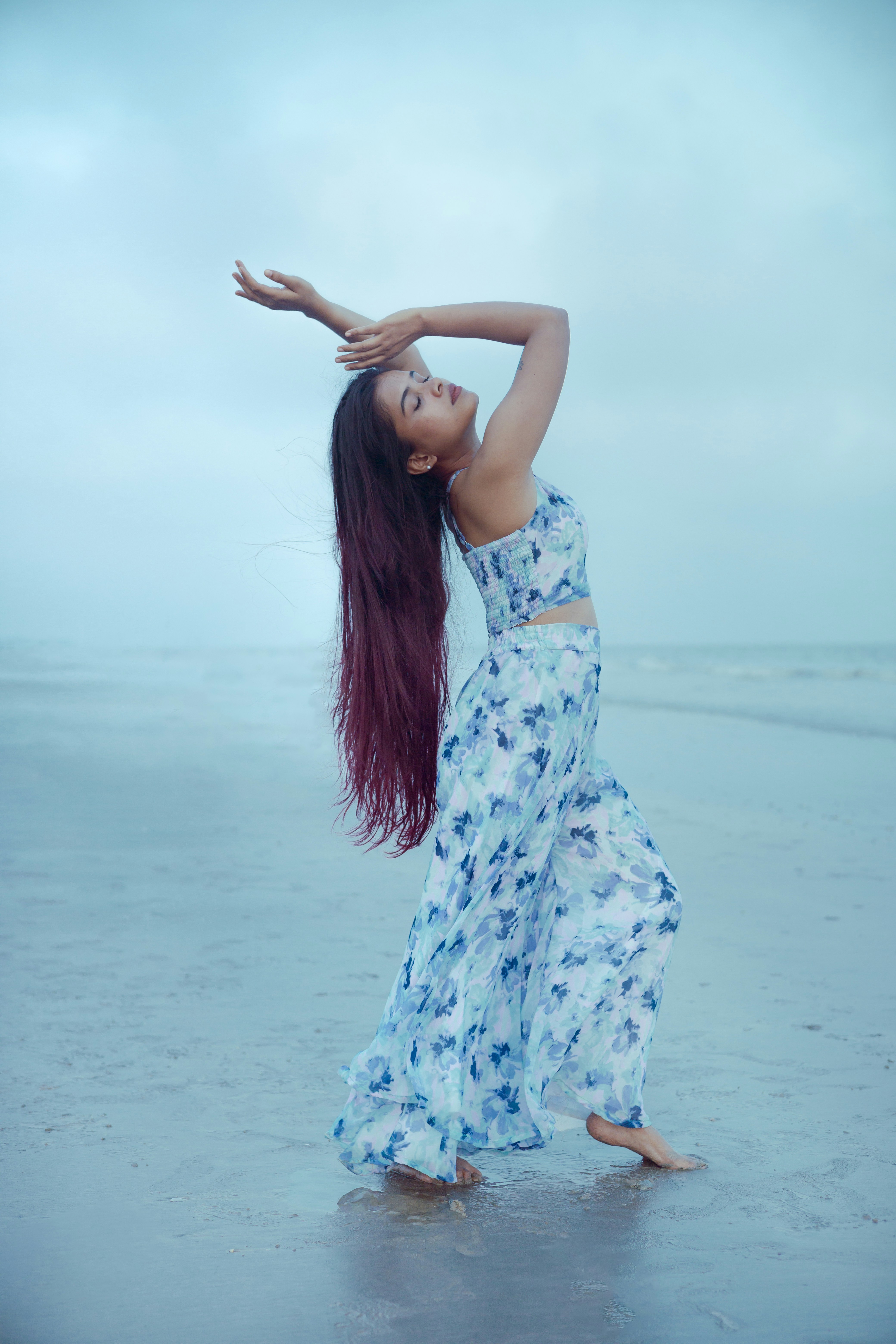 Donna in abito floreale balla su una spiaggia.