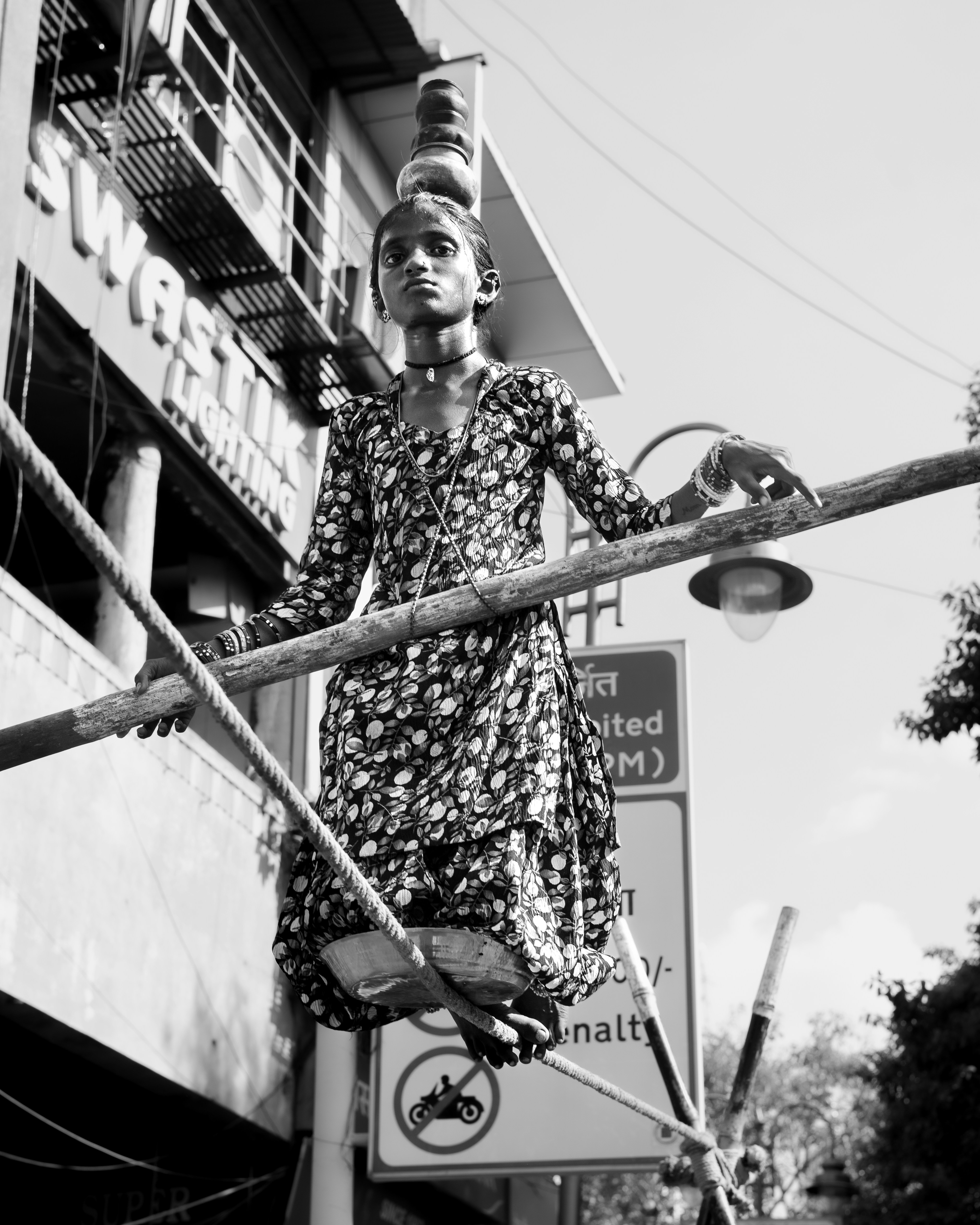 Young girl balances on a tightrope with pots on head