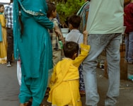 A child in yellow reaches for an adult's leg.
