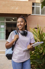 A smiling student with backpack and books walks outside.