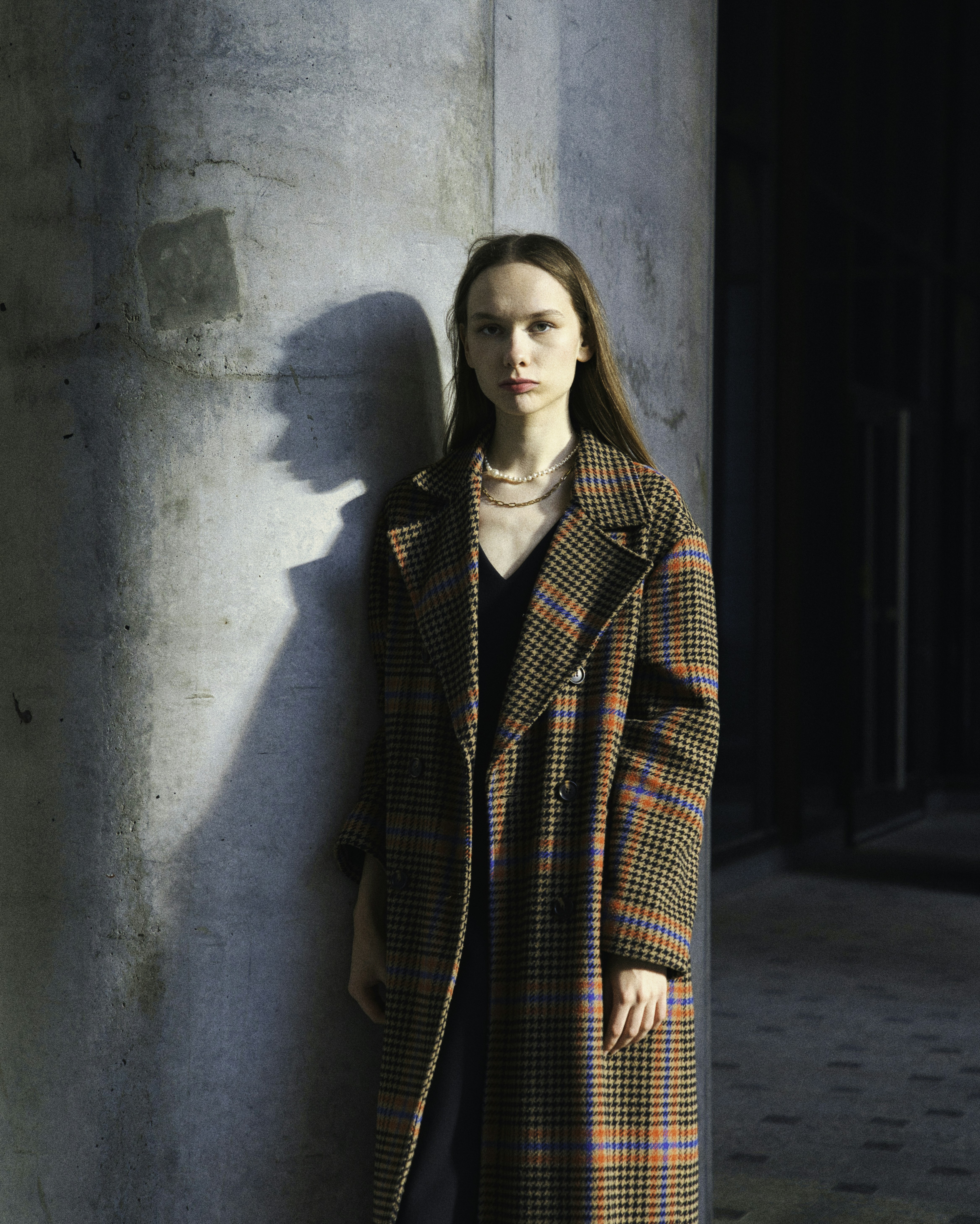 Woman in plaid coat stands by concrete pillar