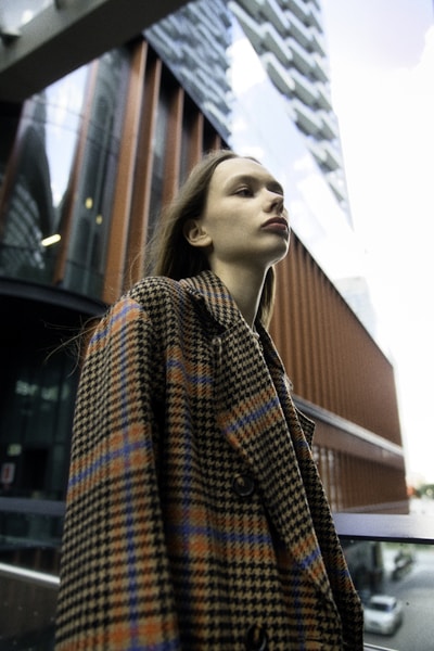 Young woman in plaid coat near modern building