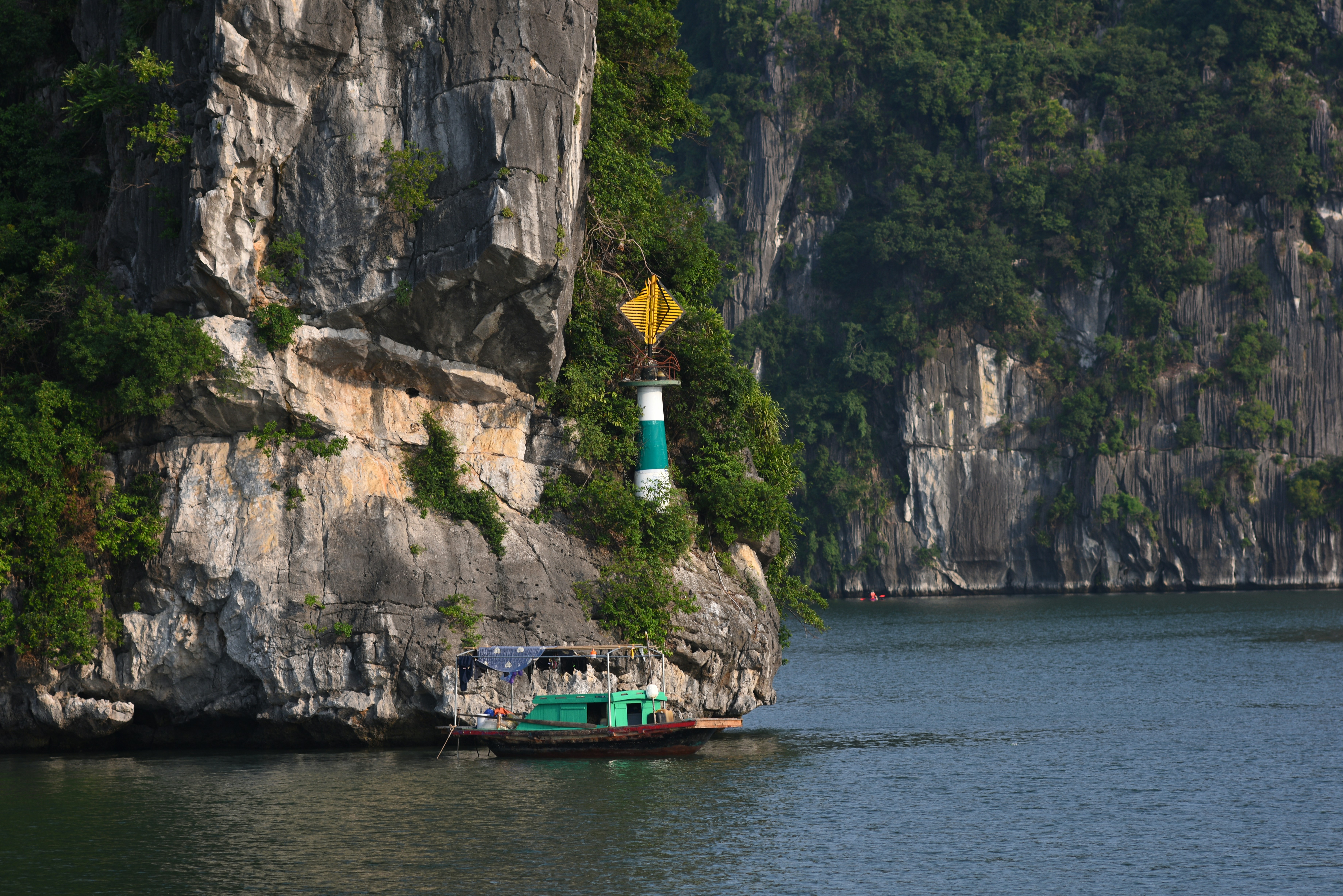 Green boat passes limestone cliffs by the sea.