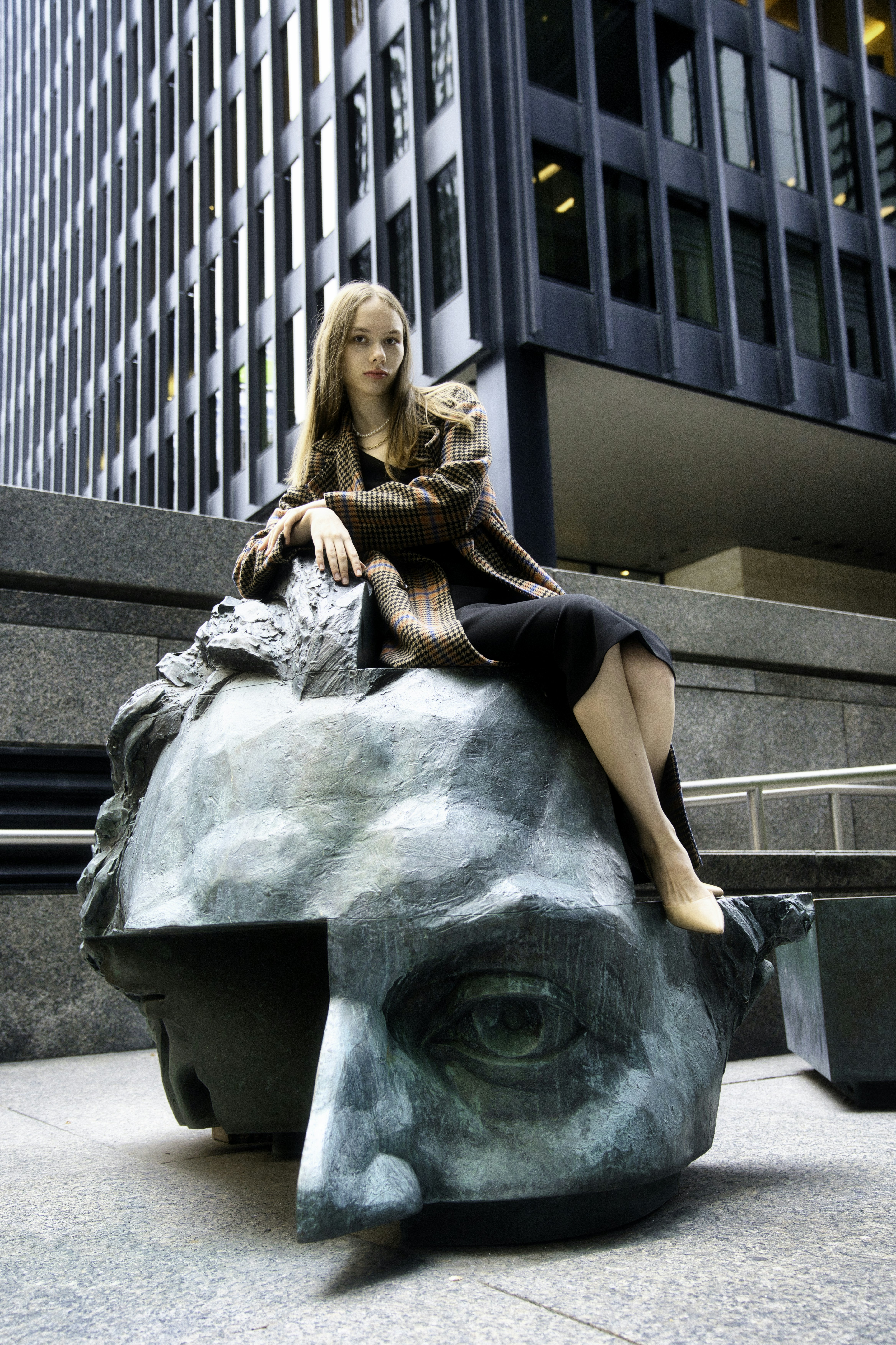 Woman sitting on a large bronze head sculpture