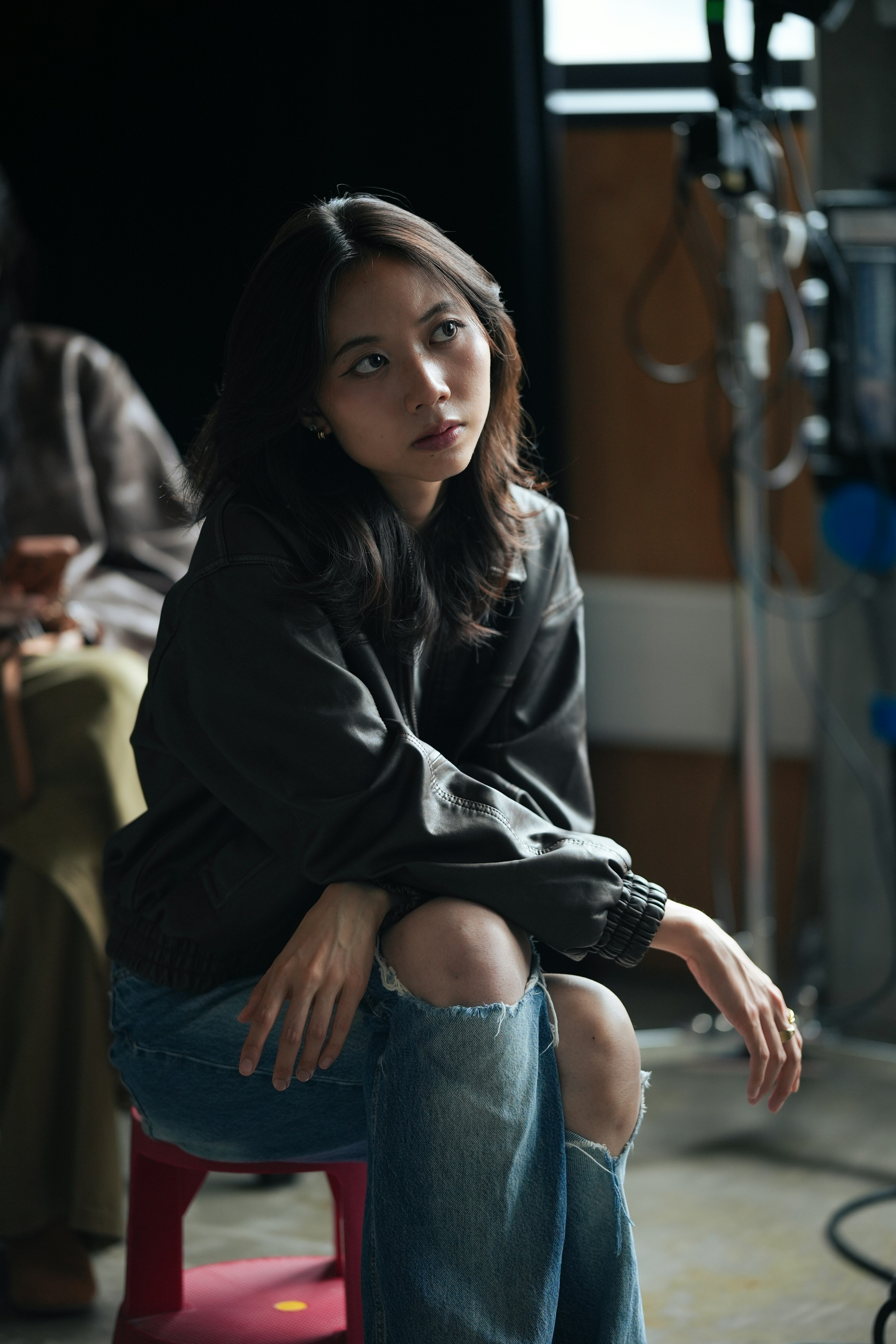 Una giovane donna siede guardando fuori dalla telecamera.