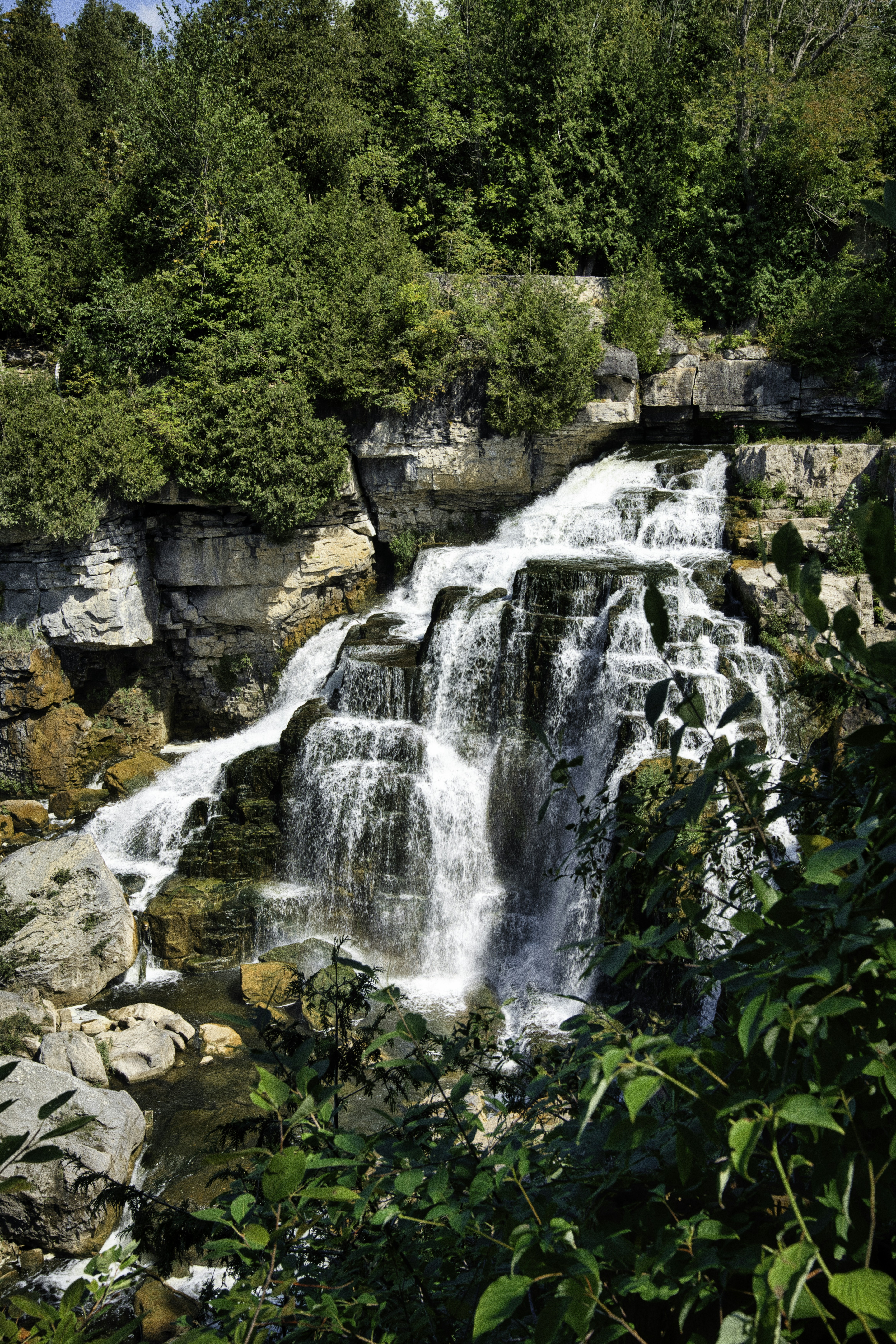 A cascading waterfall flows over rocks surrounded by trees.