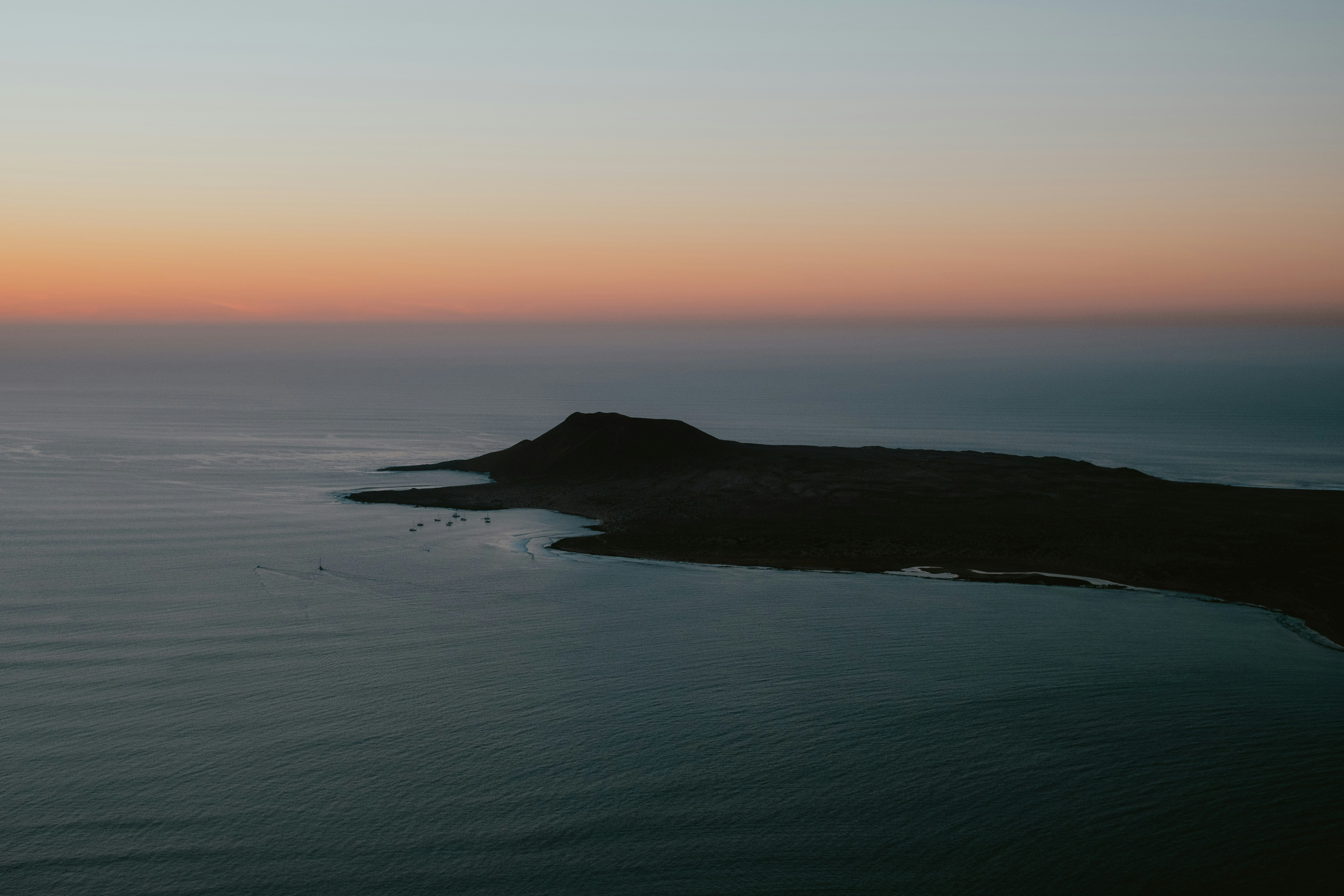 Uma silhueta escura da ilha de encontro a um oceano calmo no por do sol.
