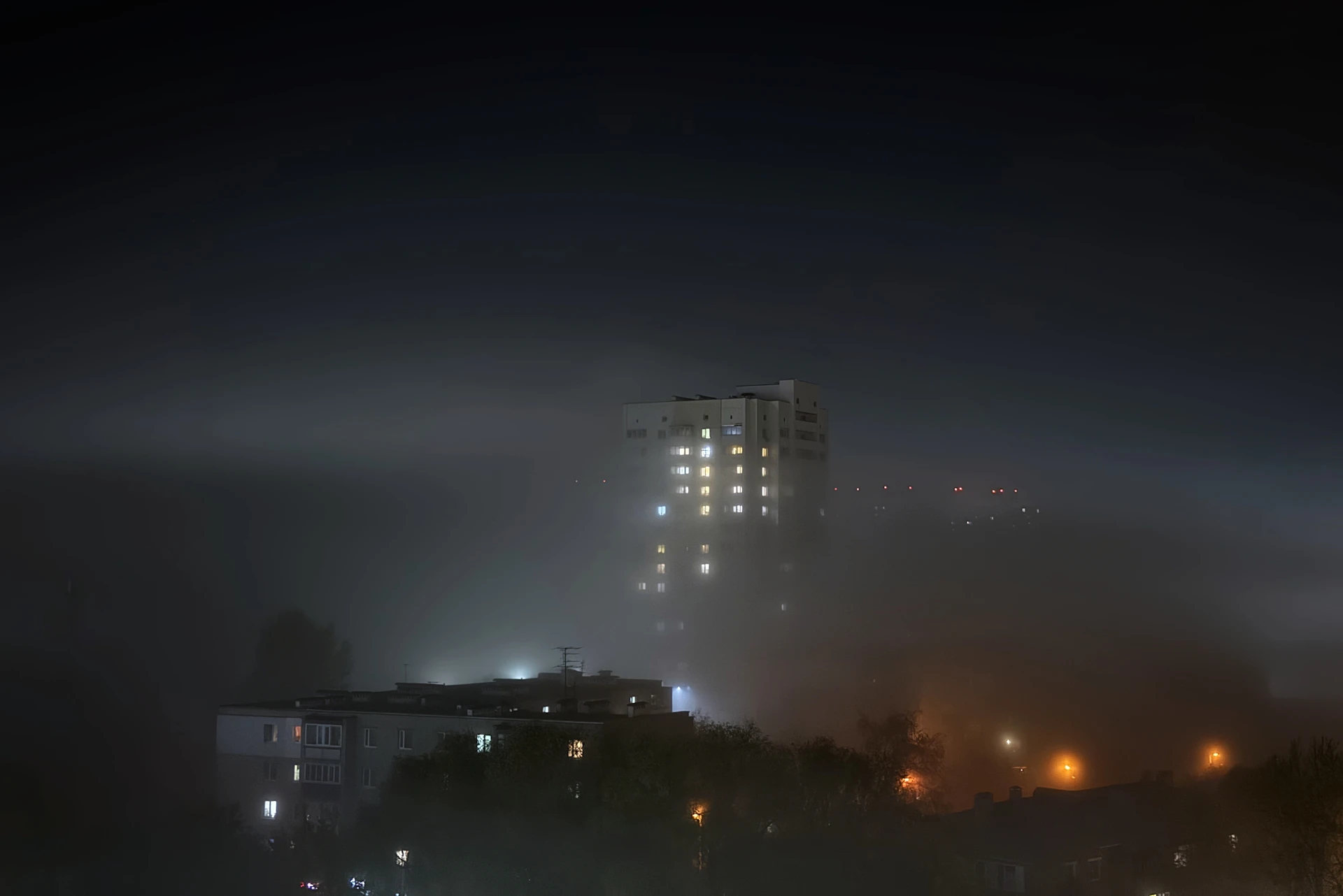 City buildings emerge from thick fog at night.
