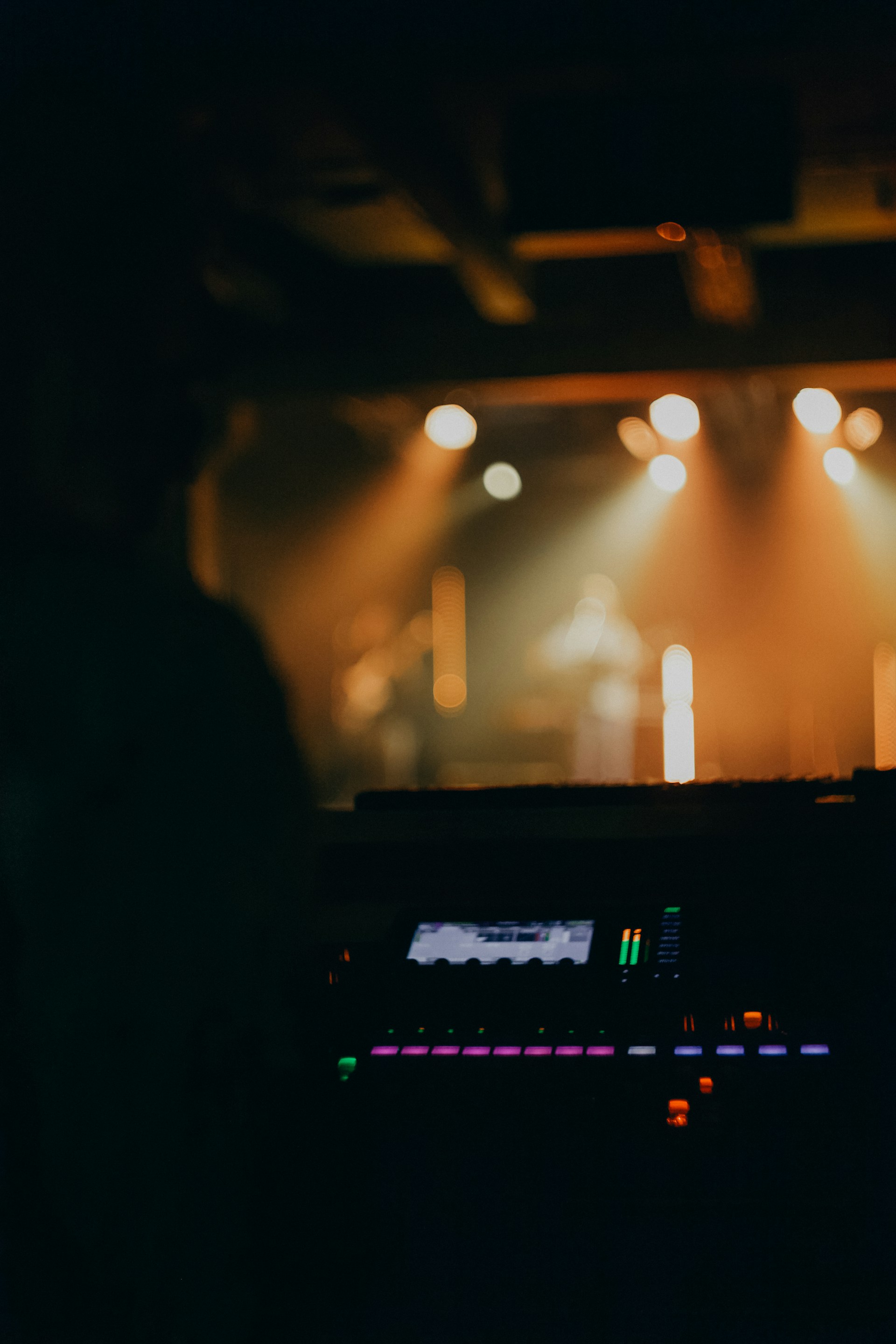 Concert stage with warm lighting and soundboard in foreground