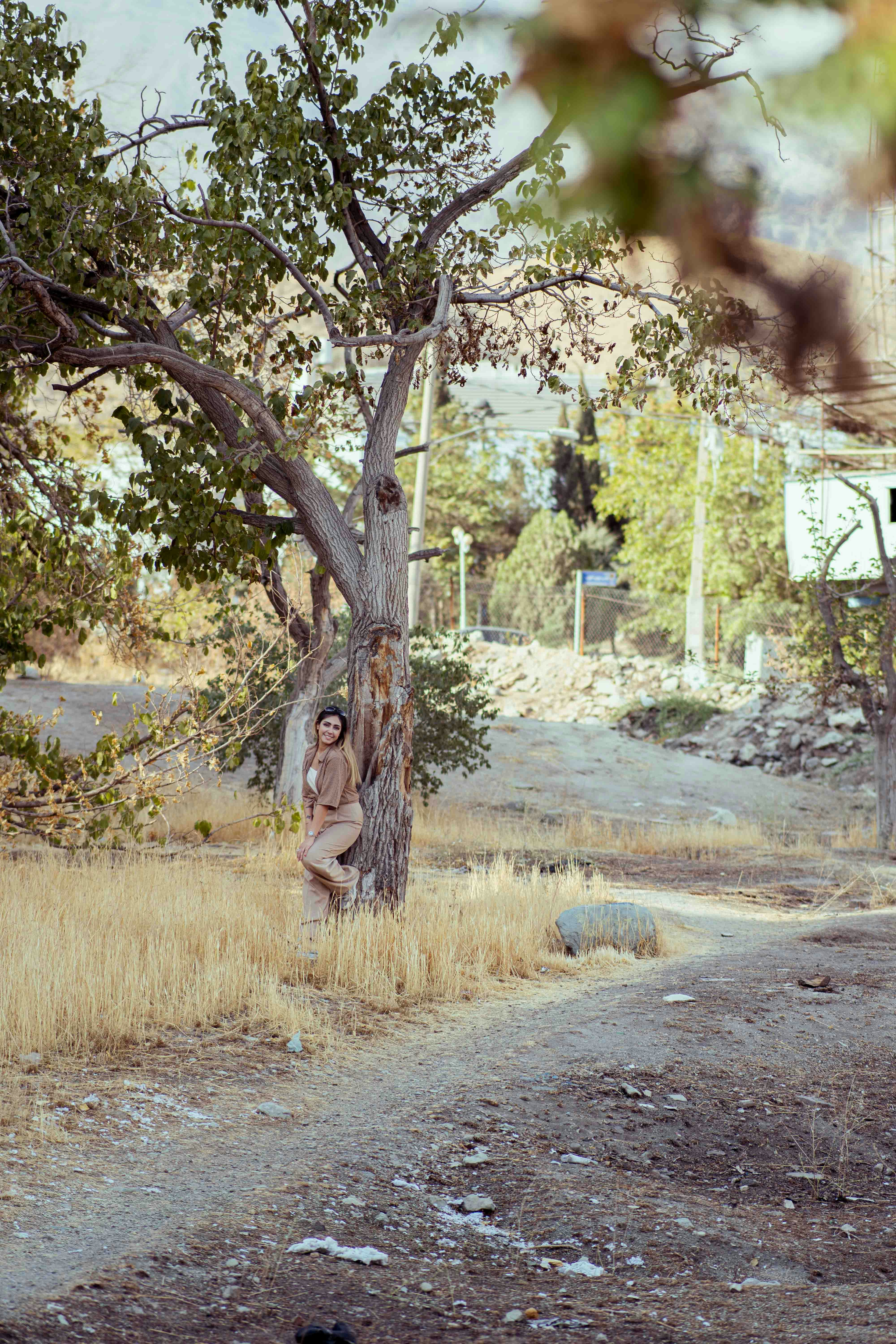 Woman leaning against a tree in dry grass