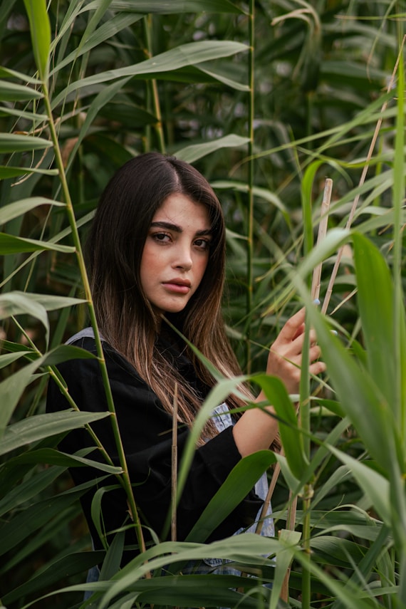 A young woman peeks through tall green reeds.