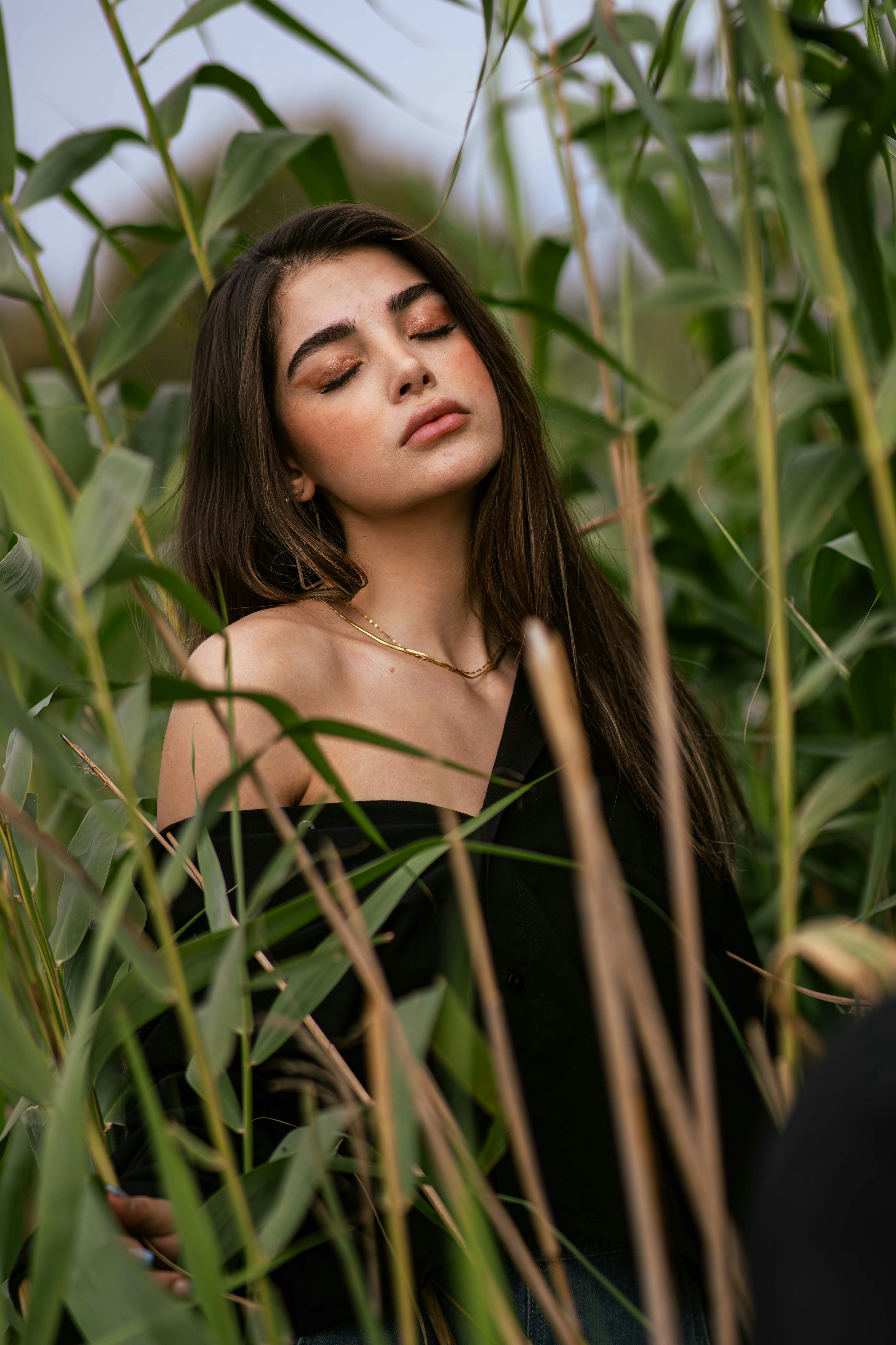 A young woman with eyes closed among tall reeds.