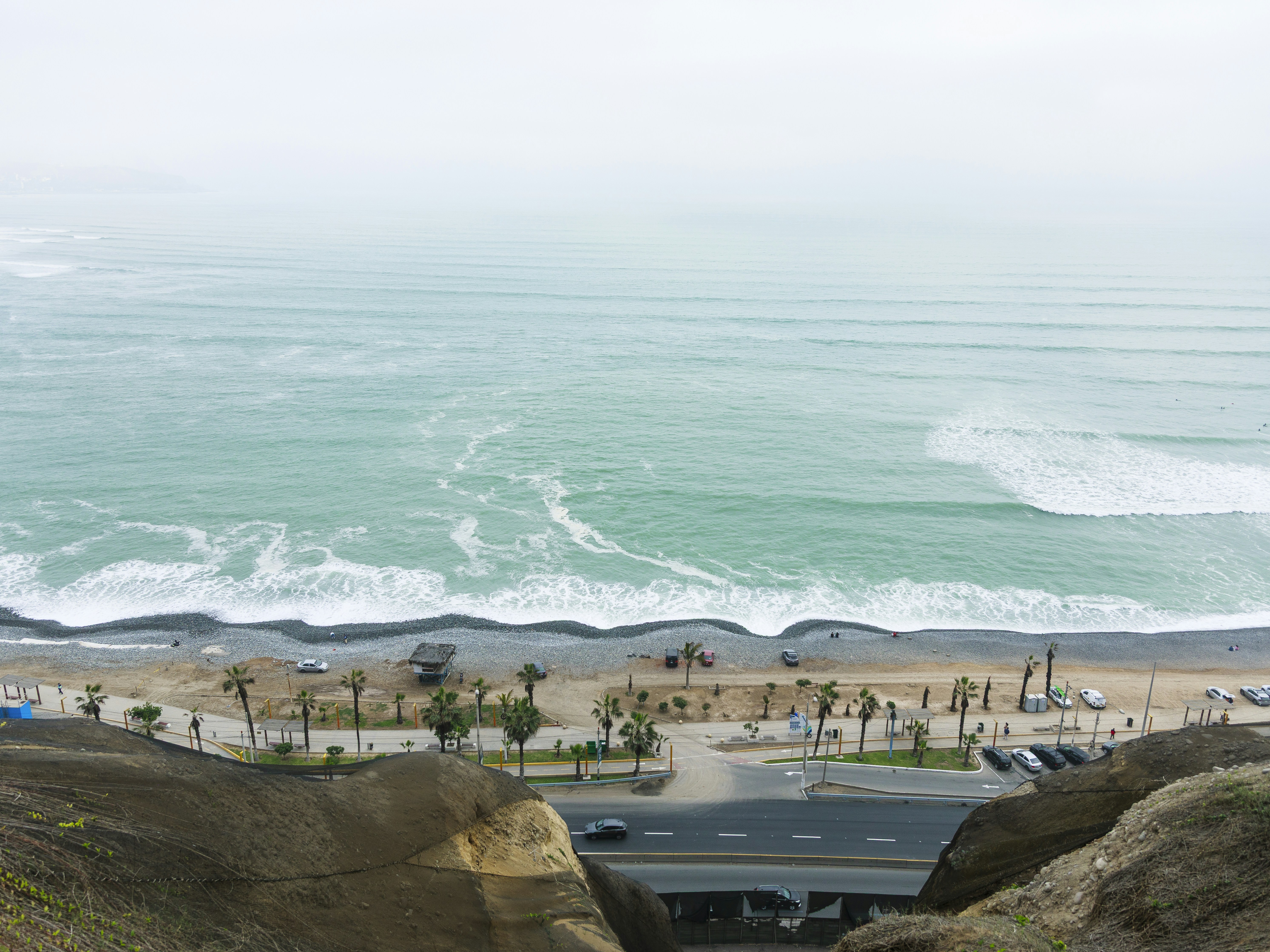 Ocean waves crash on a pebble beach with palm trees.