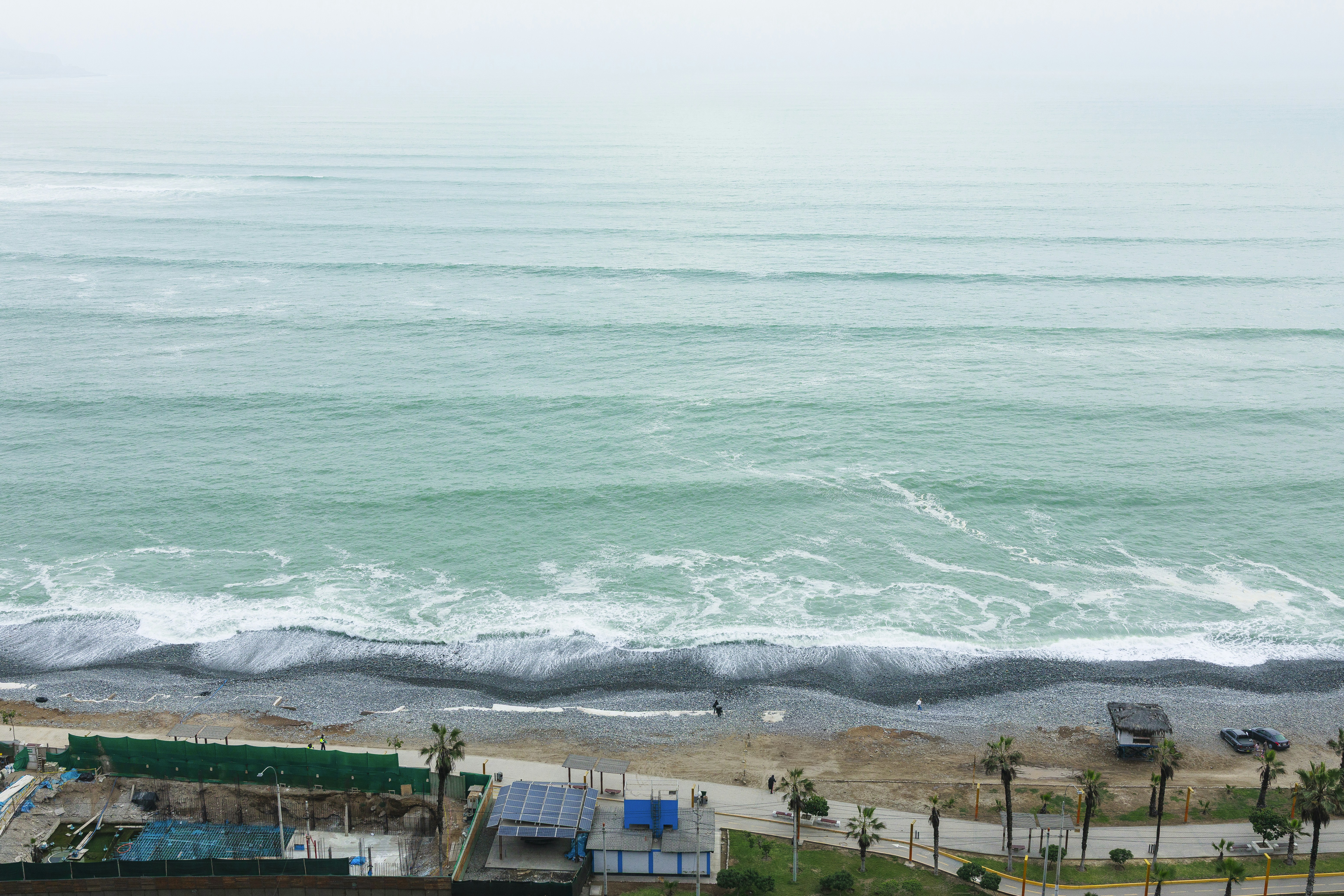 Waves crashing on a pebble beach with buildings.