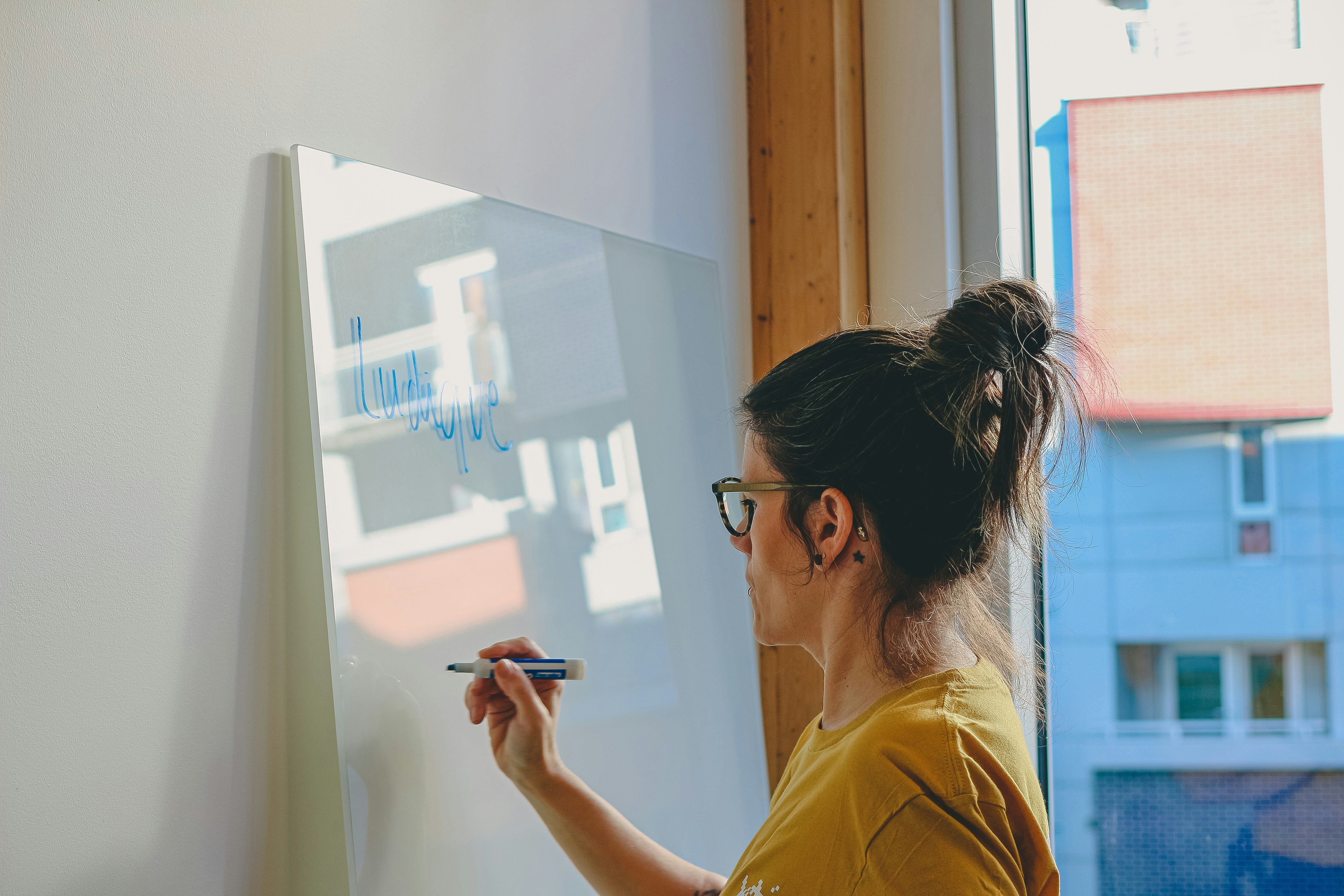 Woman writing on a whiteboard by the window.