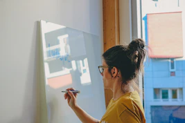 Woman writing on a whiteboard by the window.