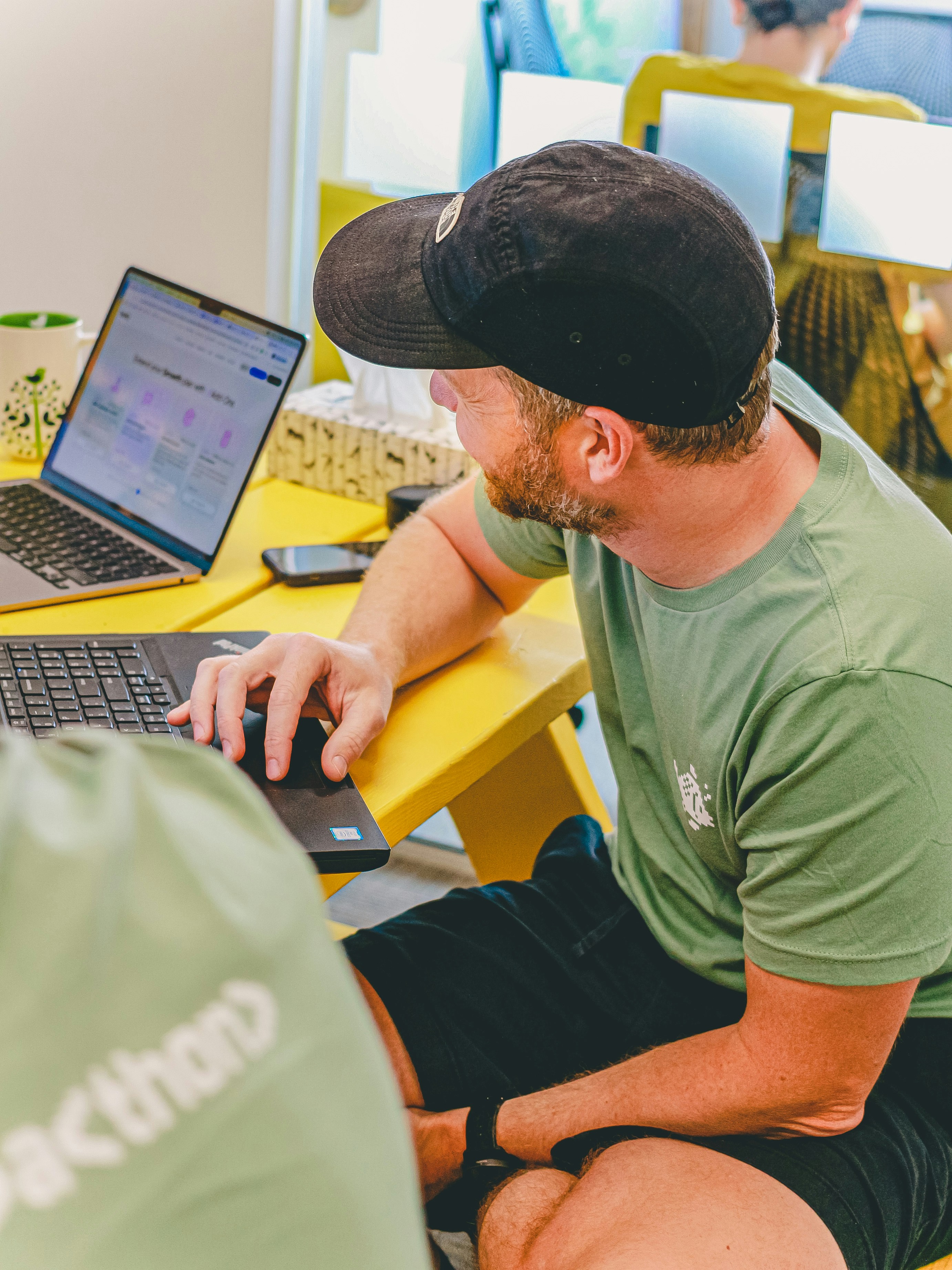 Man in hat working on laptop at yellow desk