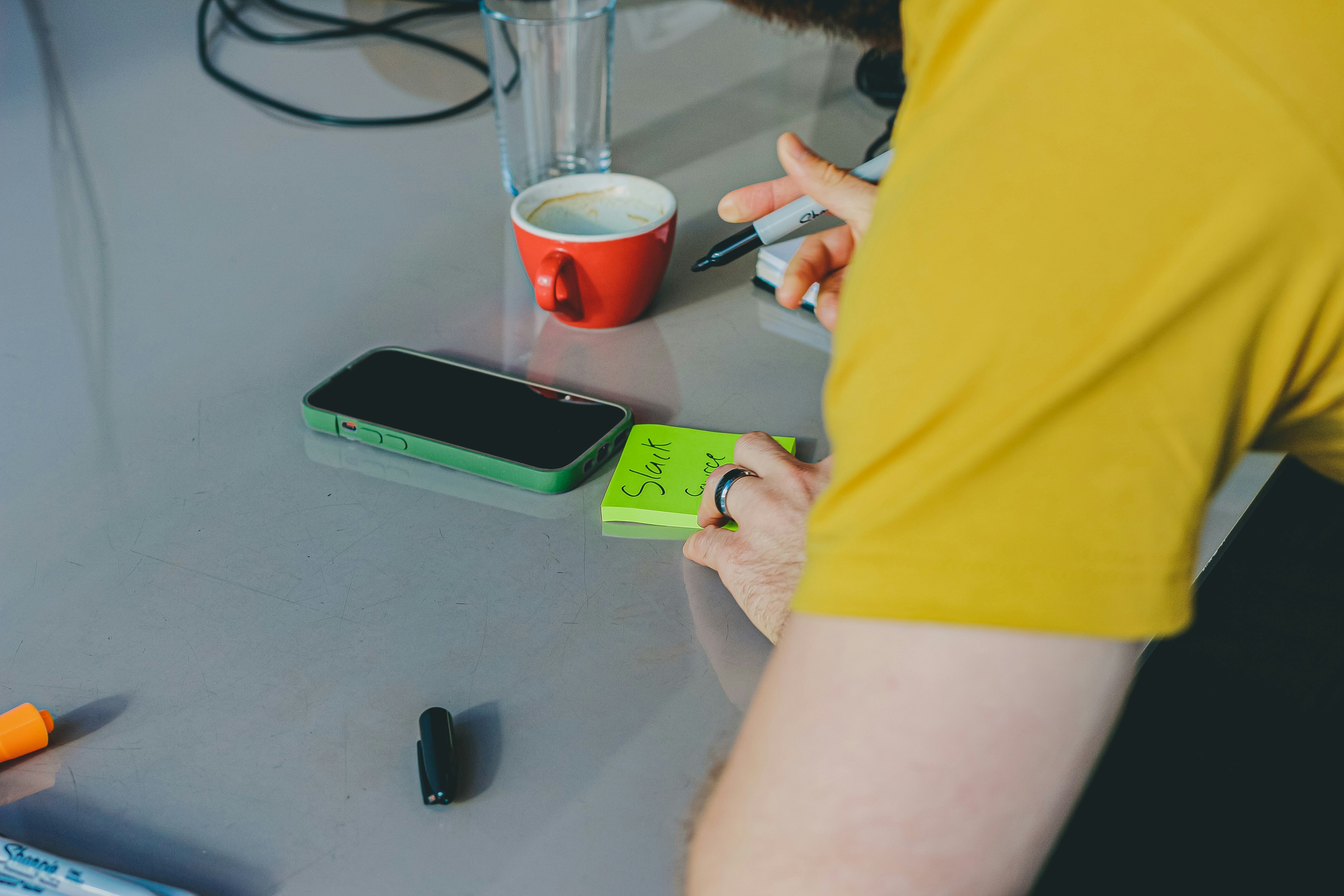 Person in yellow shirt at desk with coffee and supplies.