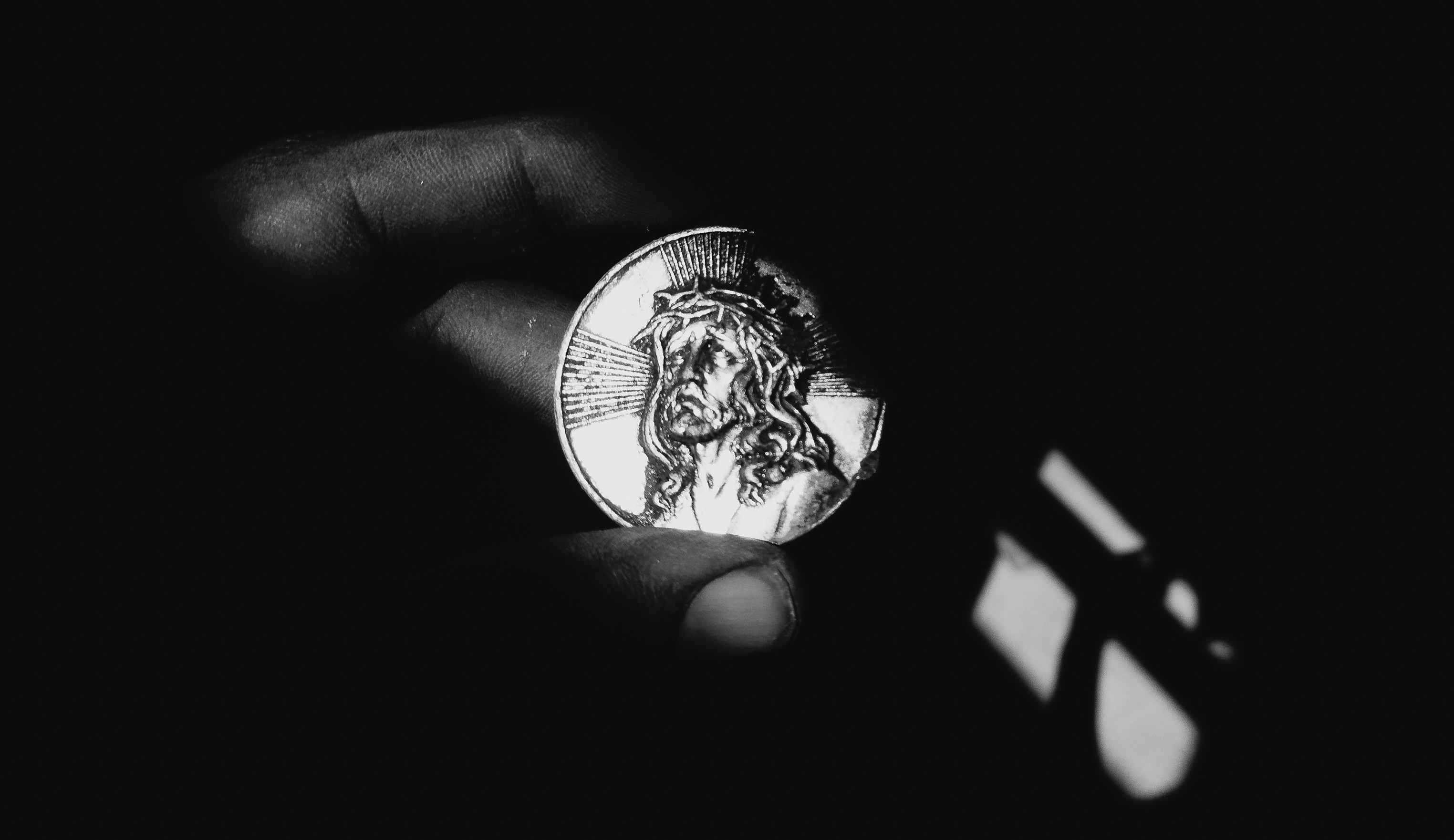 Hand holding a damaged coin with jesus' face.