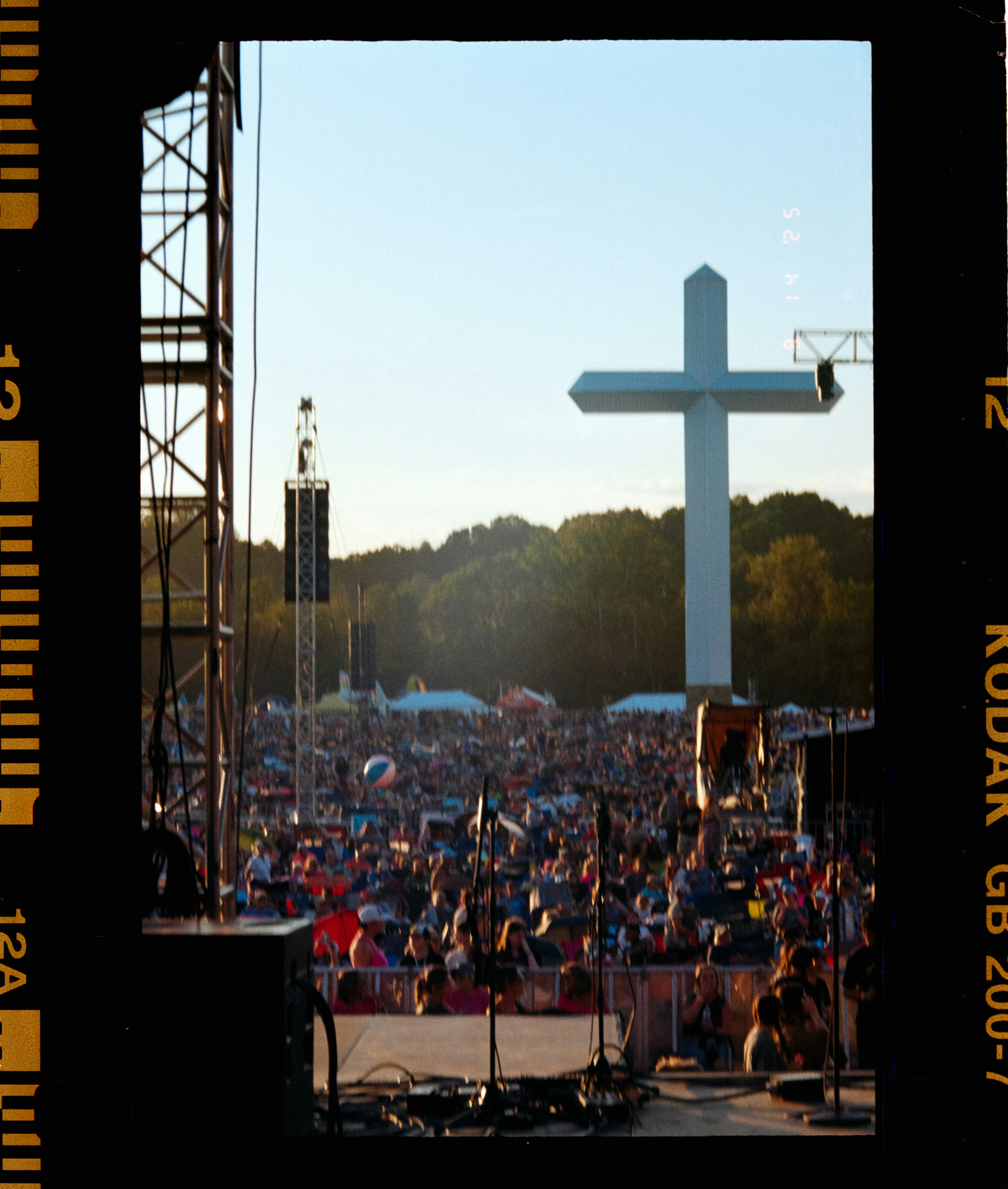 Large white cross stands over outdoor concert crowd
