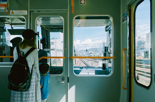 走る列車の窓ぎわに座り、流れていく景色を眺める人の後ろ姿。まとまった時間でしか成立しない移動を象徴するイメージ