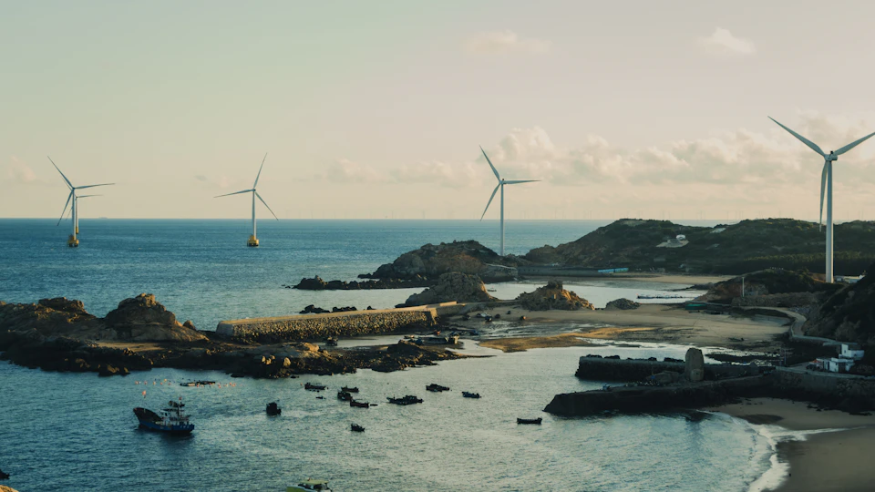 Three wind turbines stand tall on the water, harnessing wind power near rocky shoreline