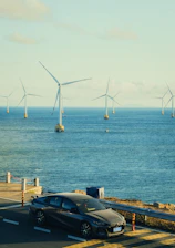 Car on road with offshore wind turbines in ocean.