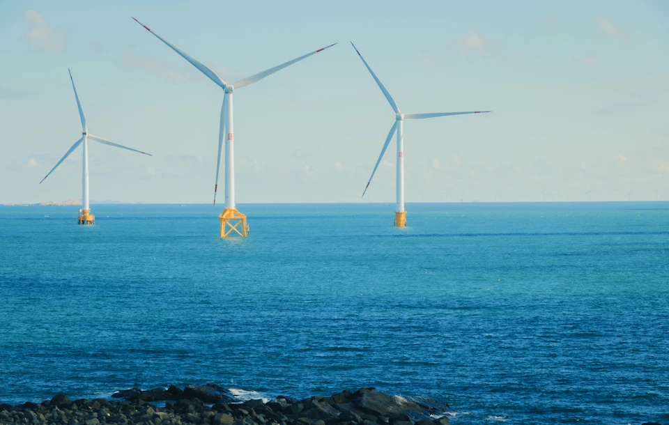 Three white wind turbines stand on the surface with yellow buoys beneath each one