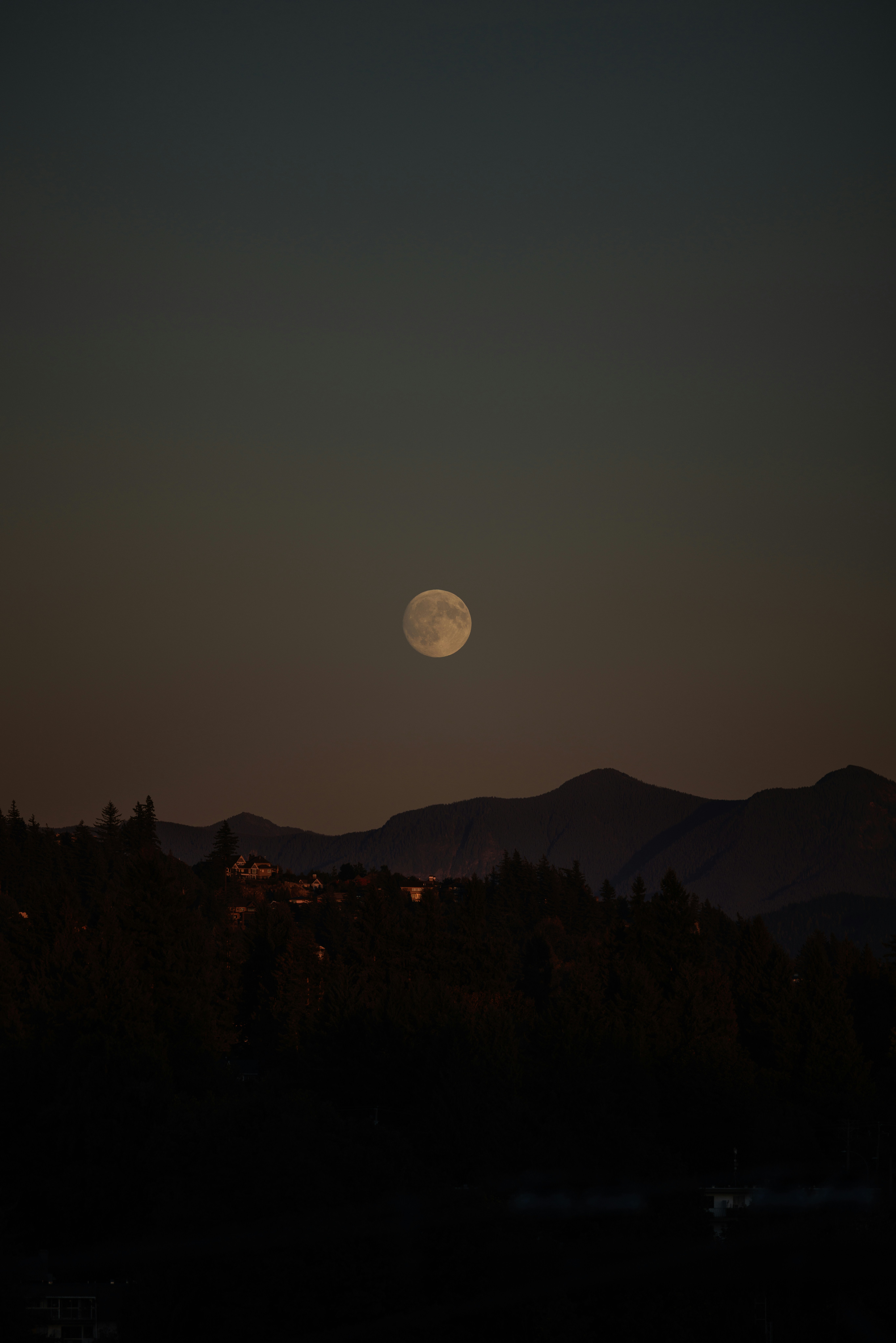 Full moon rises over dark mountains at dusk.