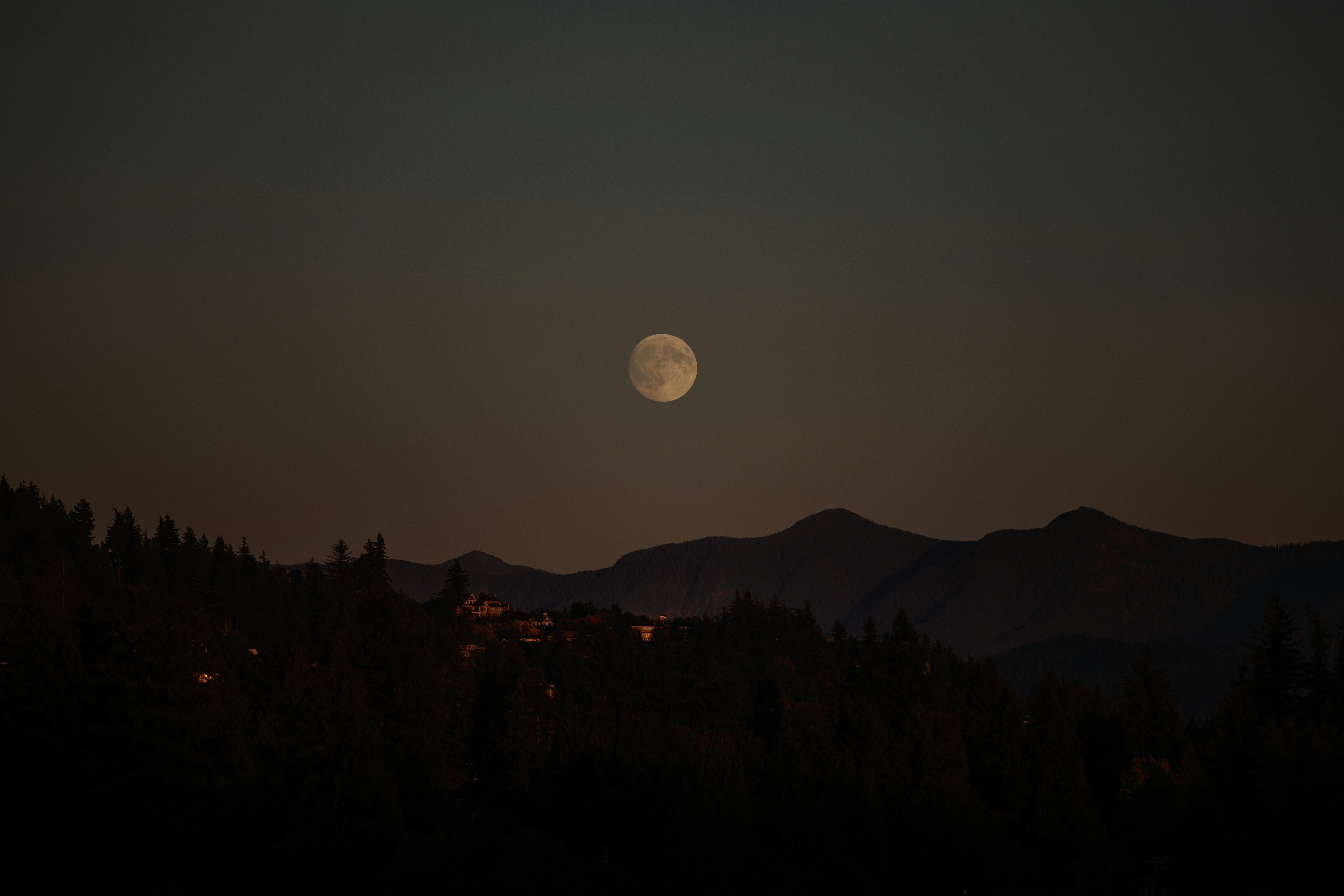 Full moon over silhouetted mountains at night.