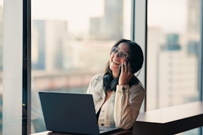 Woman talking on phone near laptop by window
