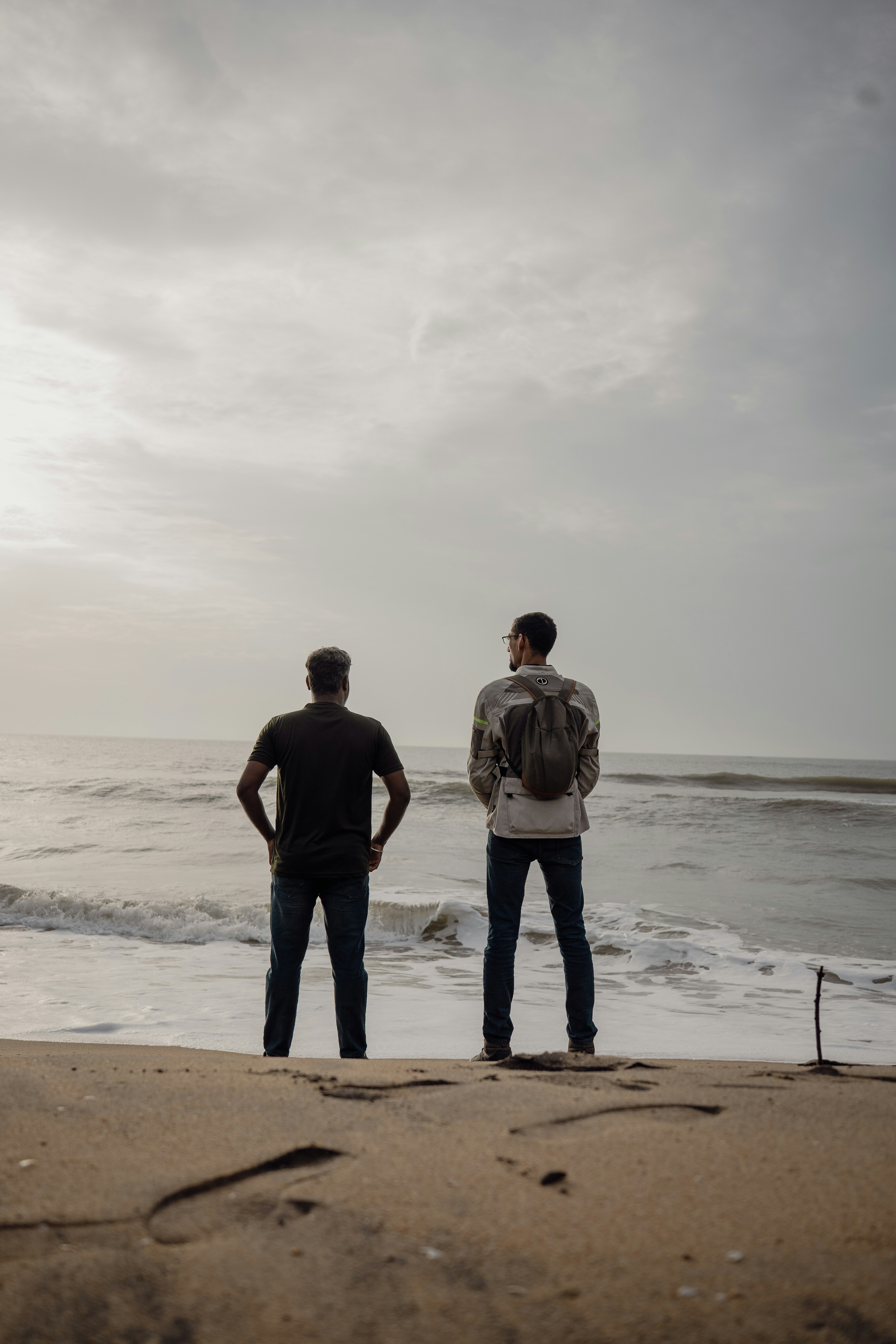 Two men stand on a sandy beach overlooking the ocean.